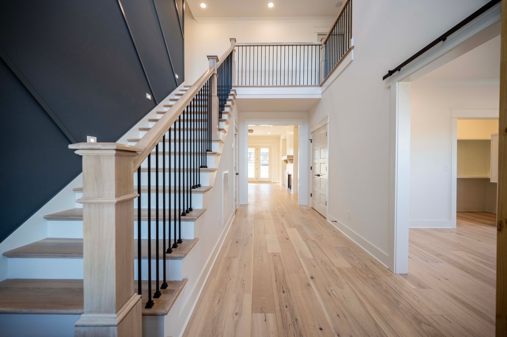 Hallway with light wood floors, a staircase with black railing, and dark blue wall.