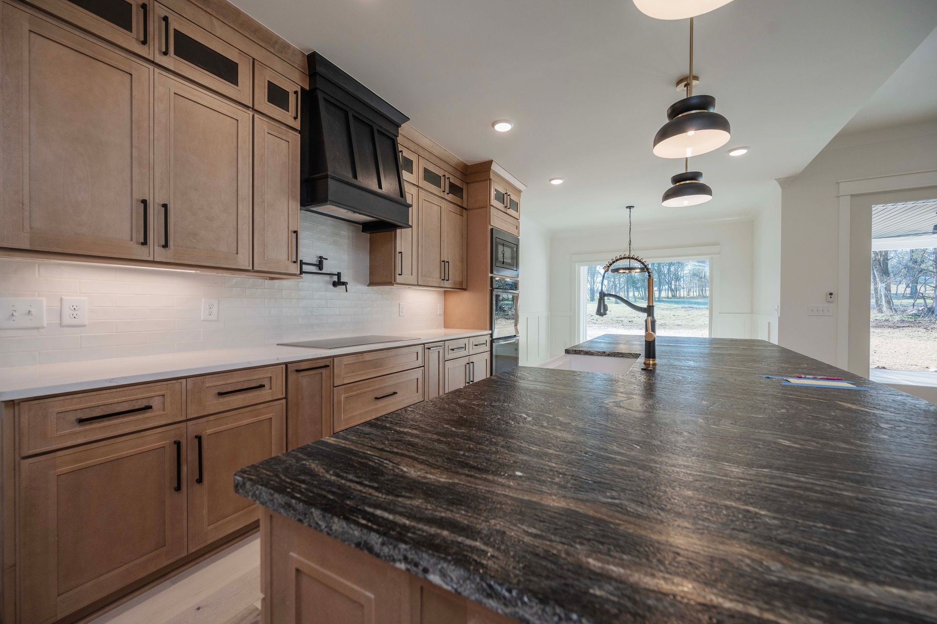 Modern kitchen with light wood cabinets, black granite island, and pendant lights.