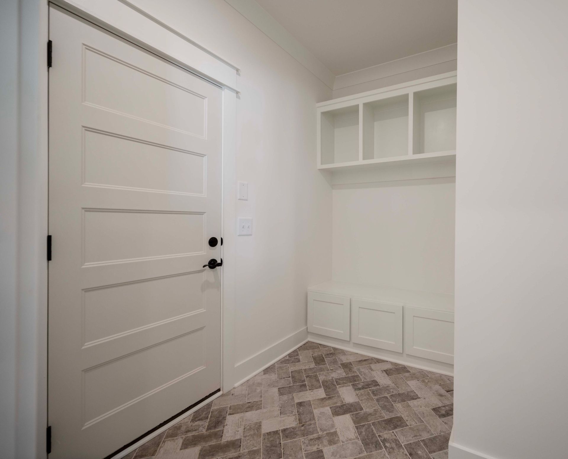 White mudroom with door, built-in bench, shelves, and herringbone floor.