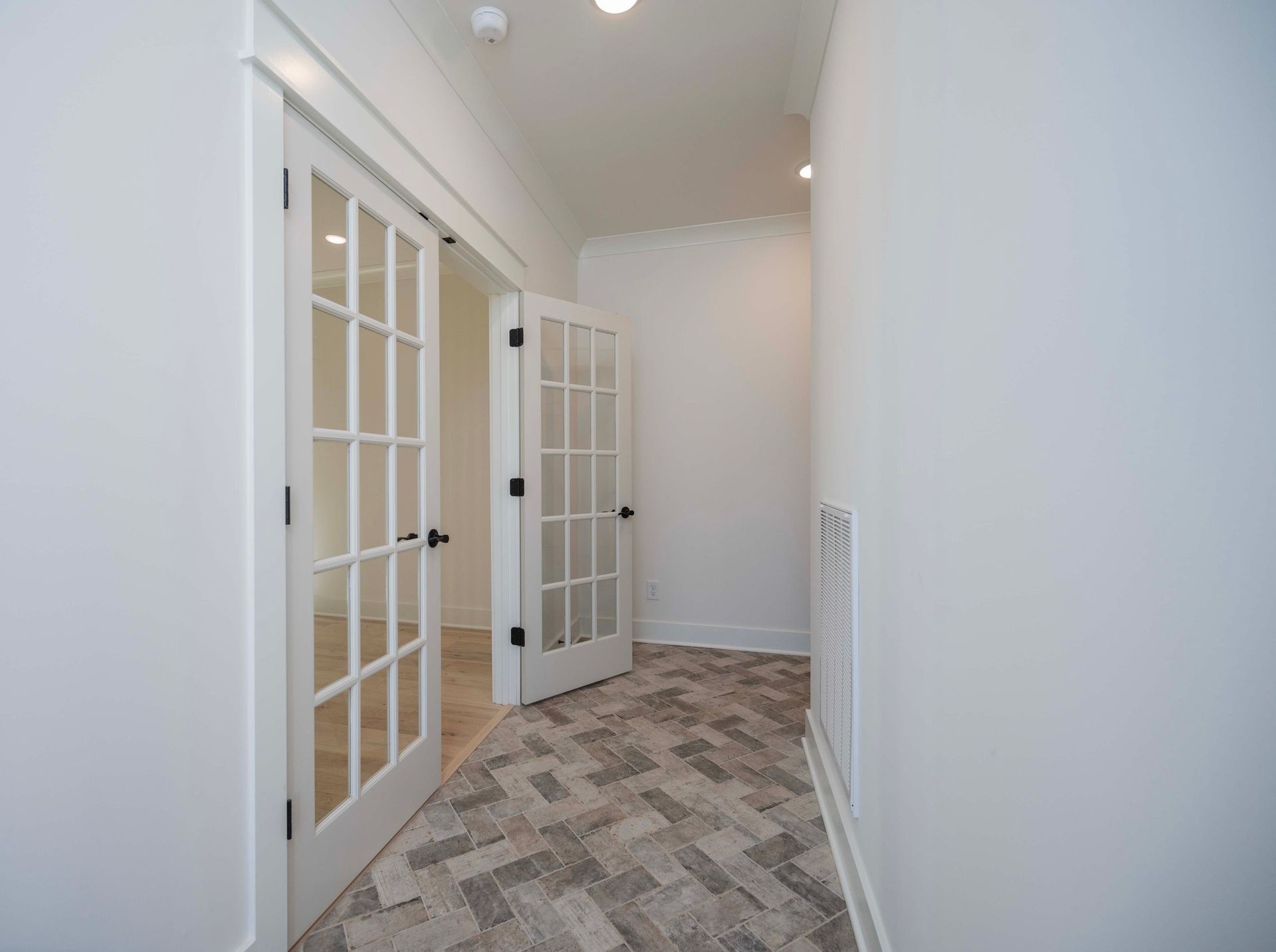Hallway with white walls, French doors, and patterned flooring.