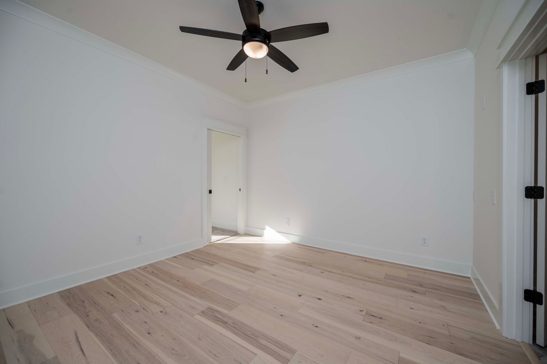 Empty room with light wood floor, white walls, ceiling fan, and open doorway.