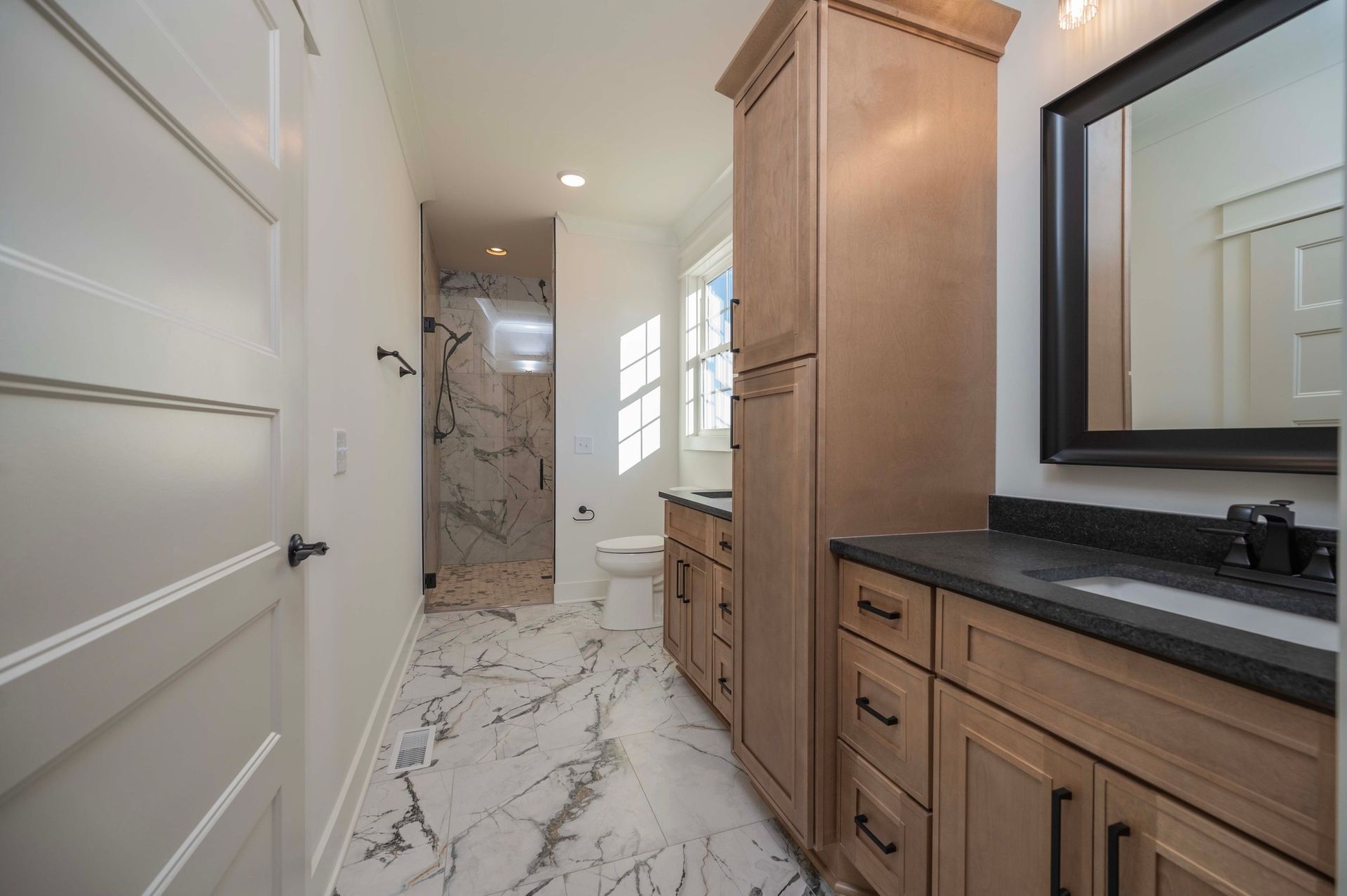 Bathroom with marble tile, light-colored cabinets, a shower, and a large mirror.
