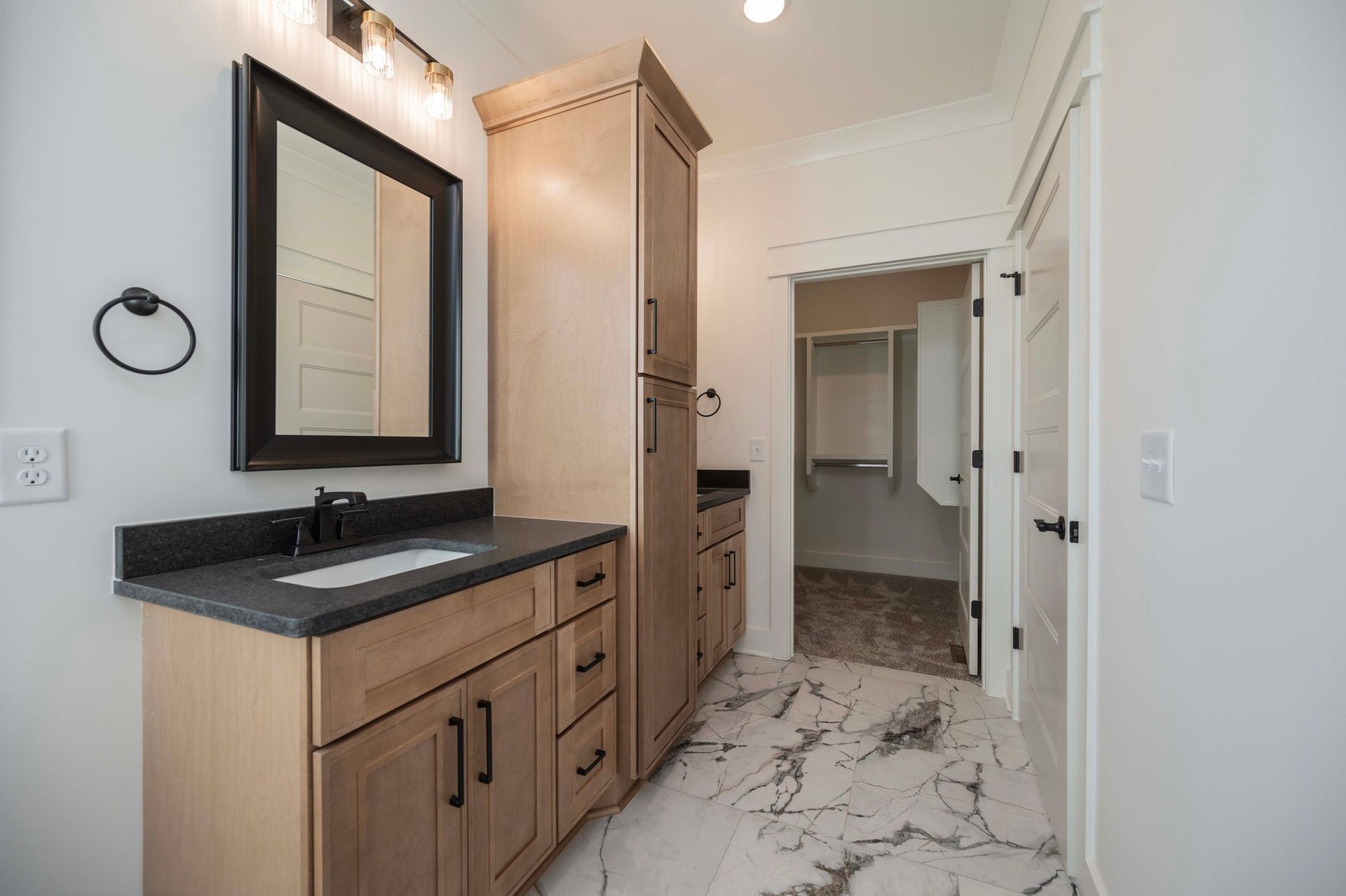 Bathroom with wood vanity, dark countertop, and marble floor leading to a closet.