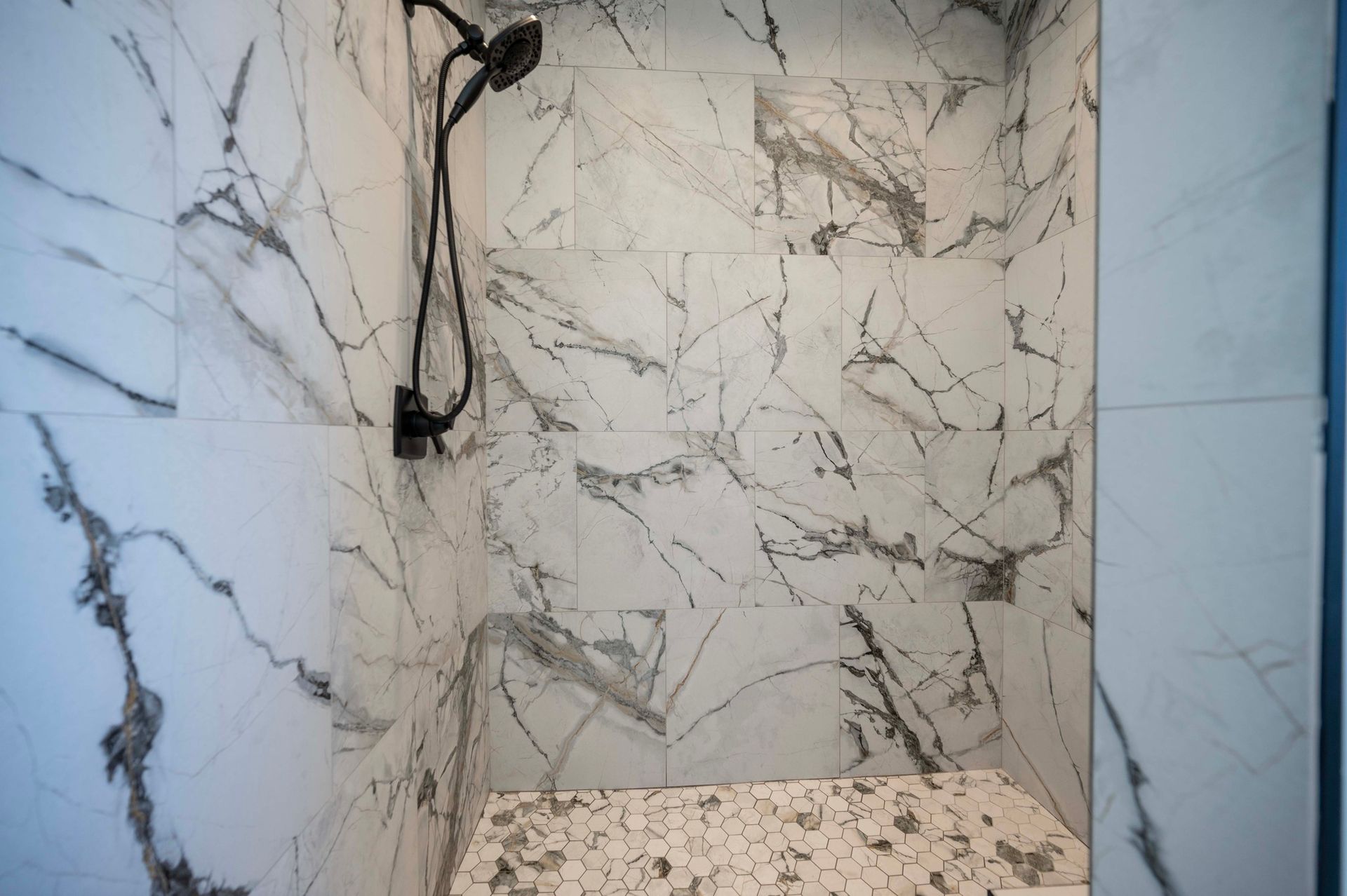 Marble-tiled shower with black showerhead. Pebble-stone floor detail.