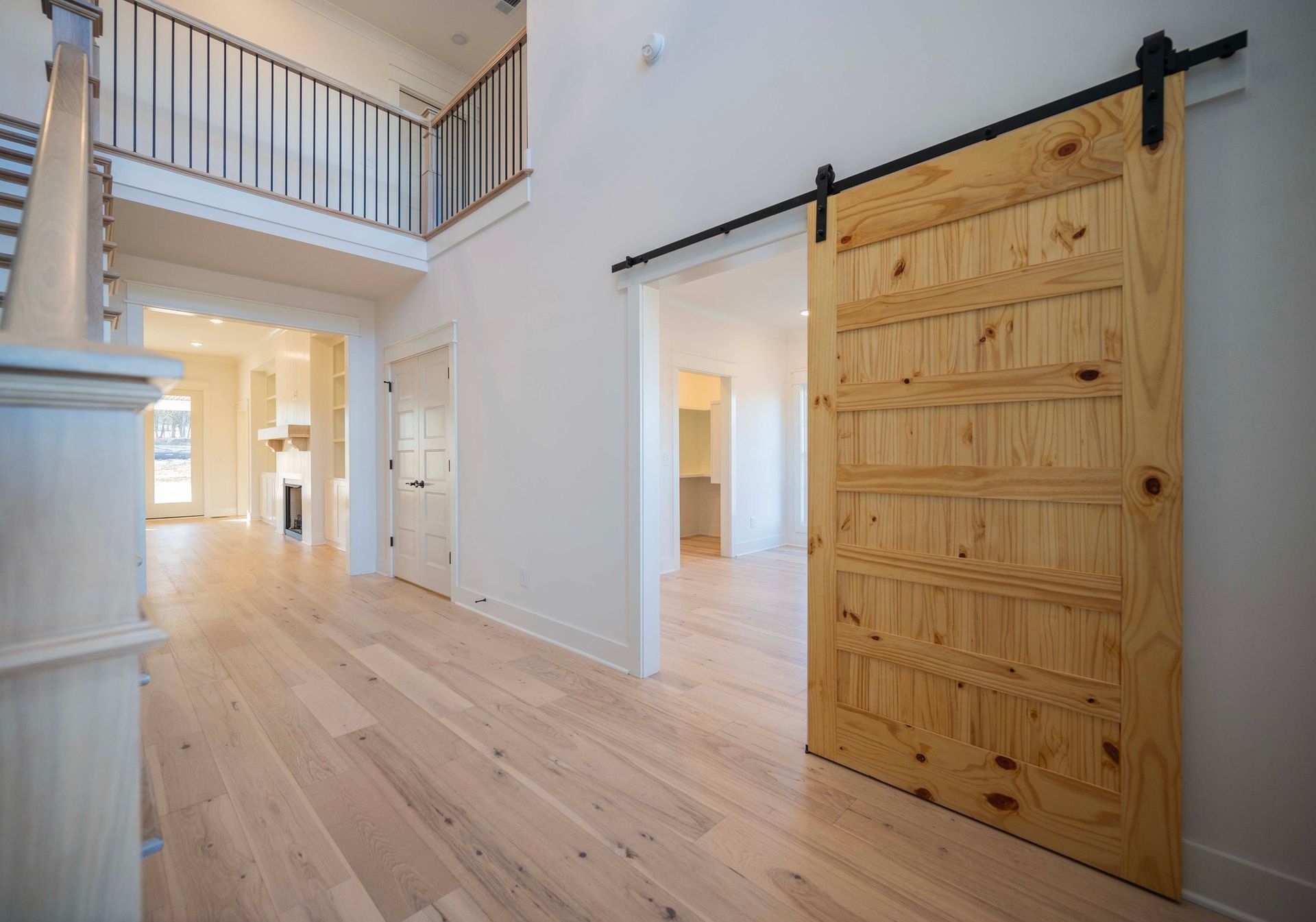 Bright interior hallway with a light wood floor, a barn door, and a staircase.