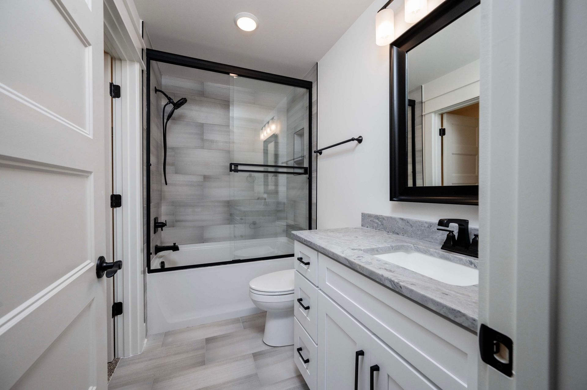 Modern white bathroom with gray stone countertop, shower, toilet, and black fixtures.