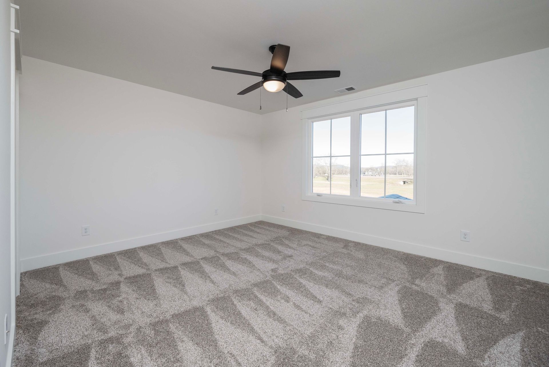 Empty bedroom with white walls, carpet, window, and ceiling fan.