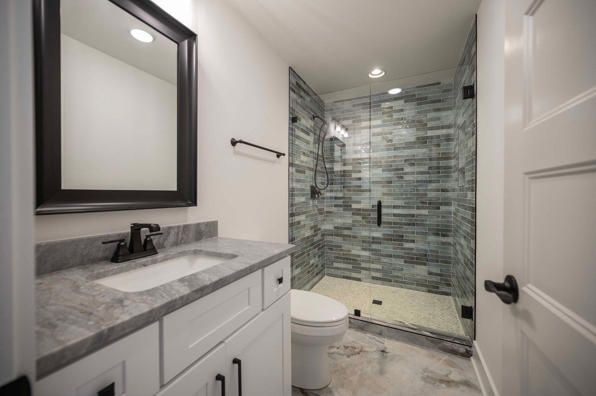 Bathroom with white vanity, gray countertop, glass shower with stone tile, and black fixtures.
