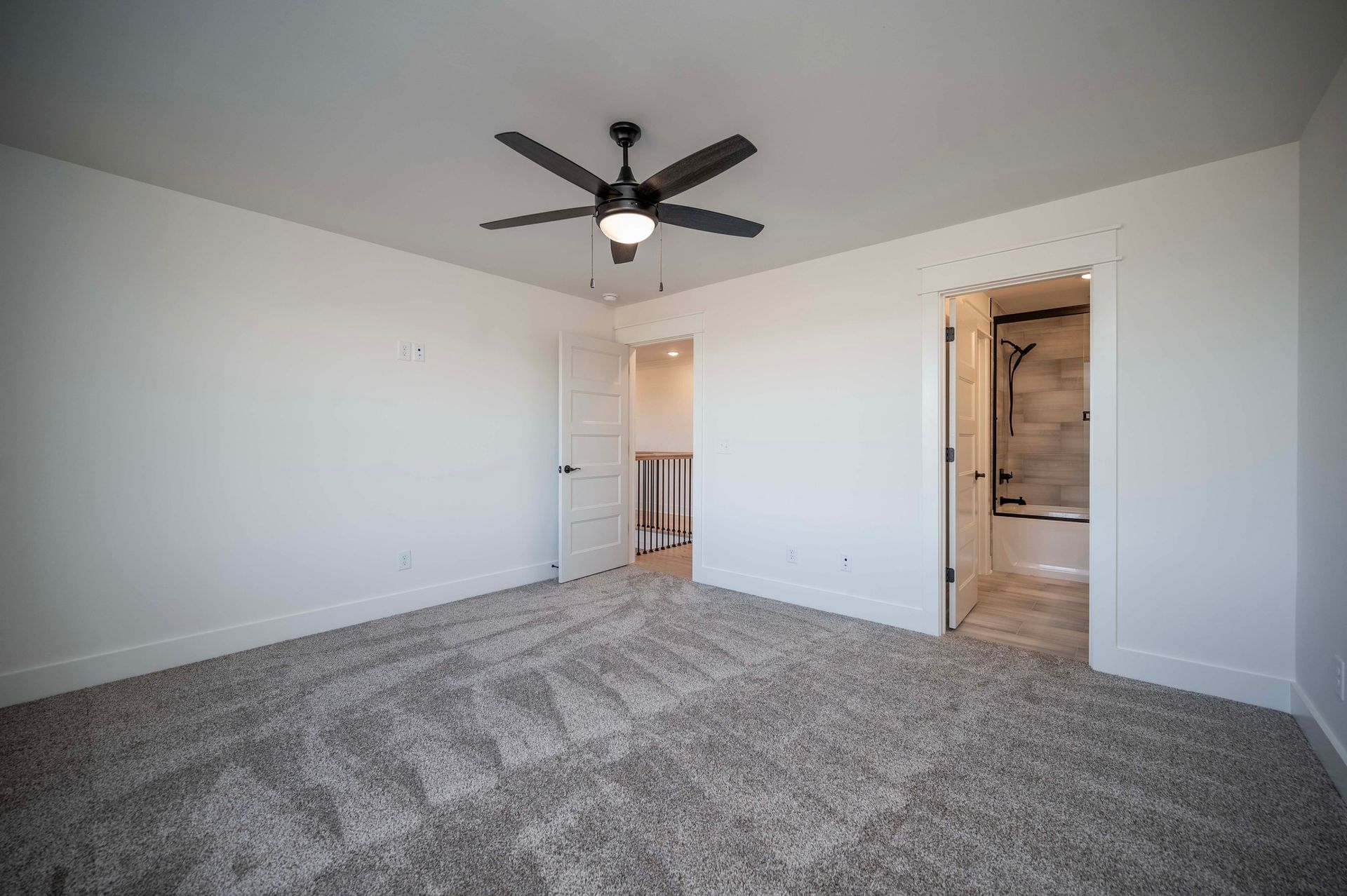 Empty room with gray carpet, white walls, ceiling fan, and doors leading to a bathroom and a small room.