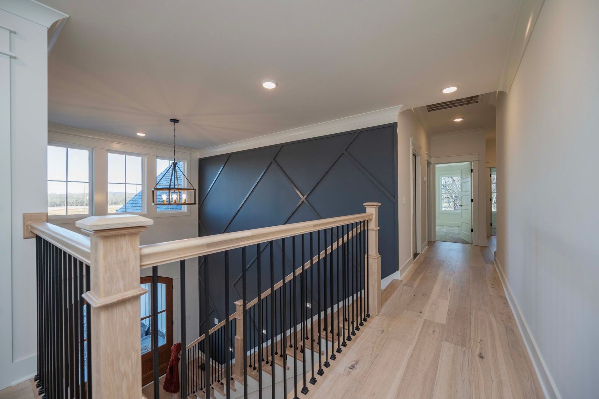 Interior view of a hallway with wood floor, black accent wall, and wooden and black metal railing.