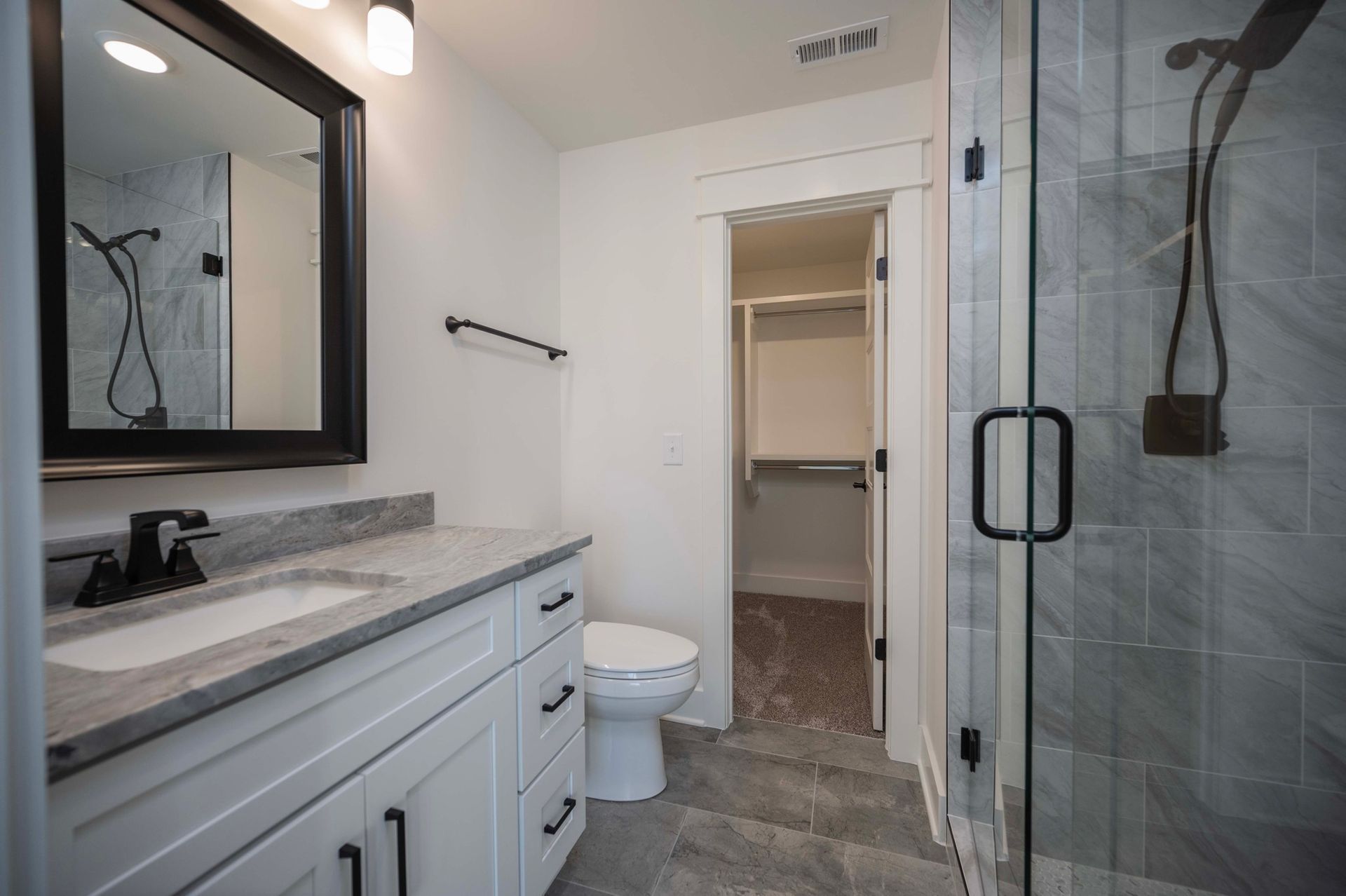 Bathroom with white vanity, gray countertop, open closet, and glass shower.