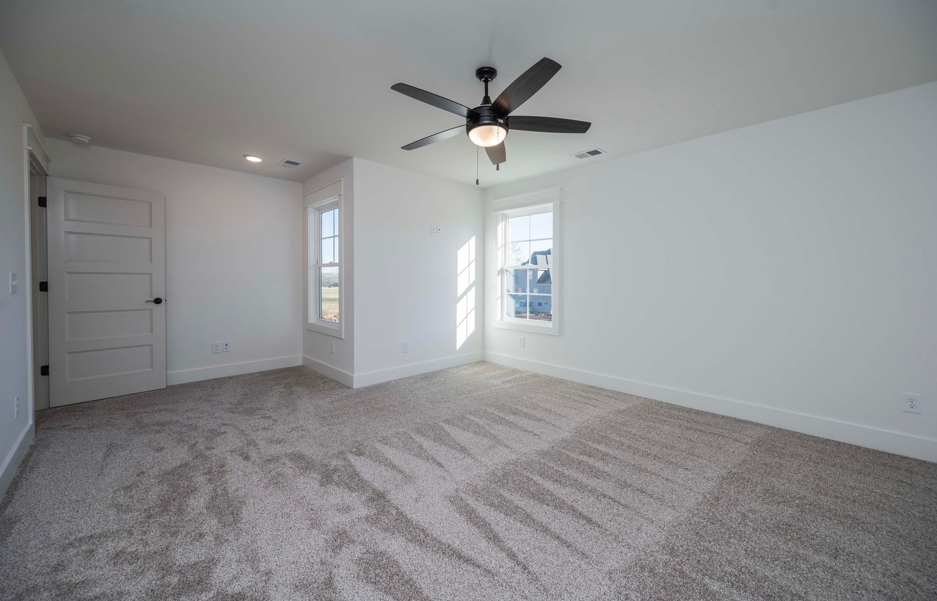 Empty bedroom with light carpet, white walls, two windows, and a ceiling fan.