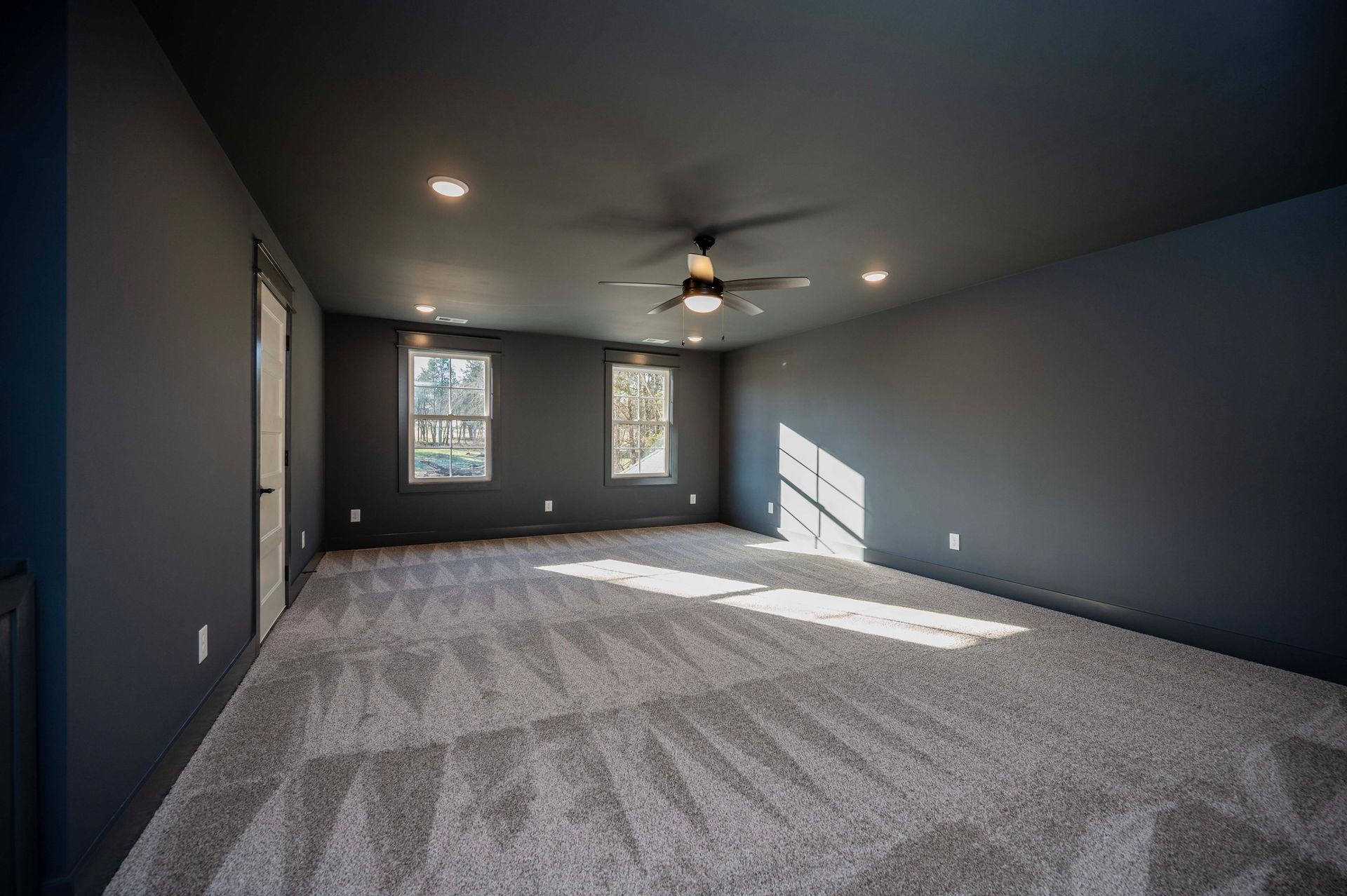 Empty room with dark gray walls, white trim, recessed lighting, carpet, windows, and ceiling fan.