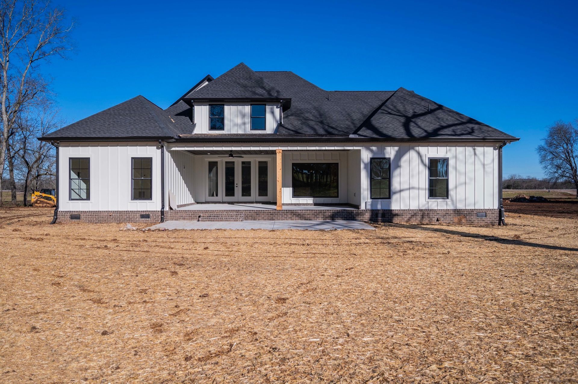 White house with black roof and windows against a clear blue sky, set on a brown, barren yard.