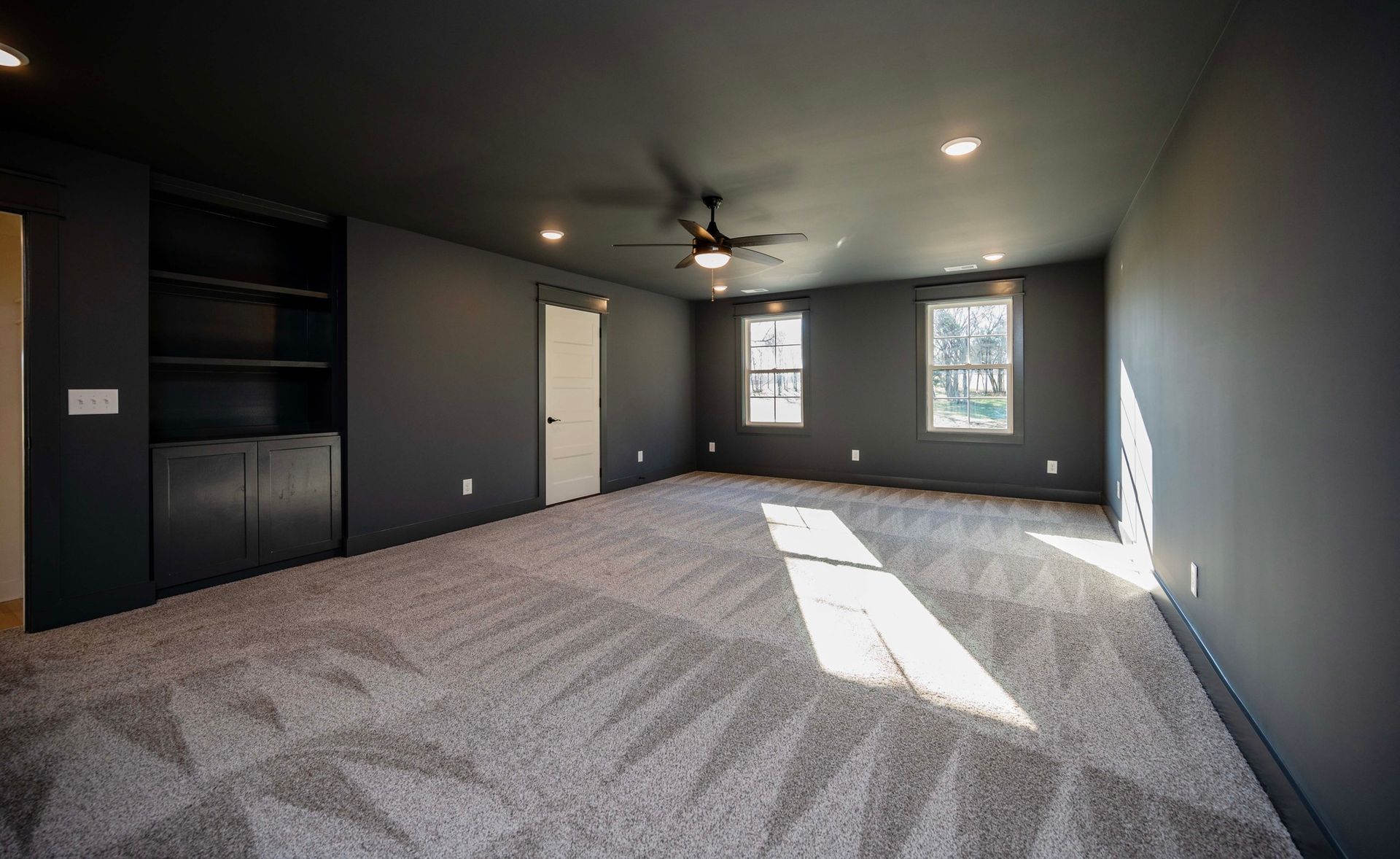 Empty room with gray walls, ceiling, and built-in storage. Light gray patterned carpet, three windows.