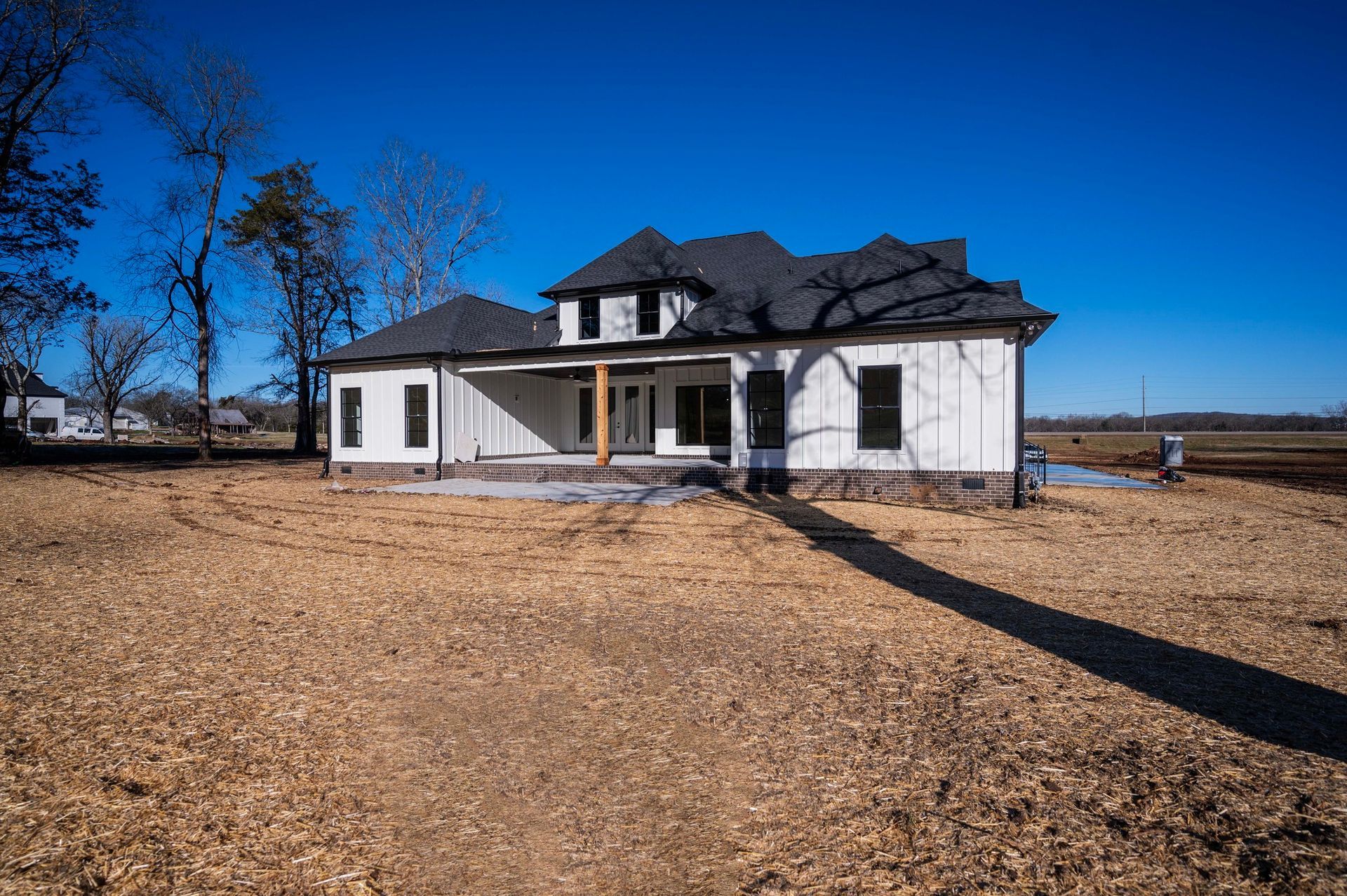 White farmhouse with black roof, set on a brown field under a clear blue sky.