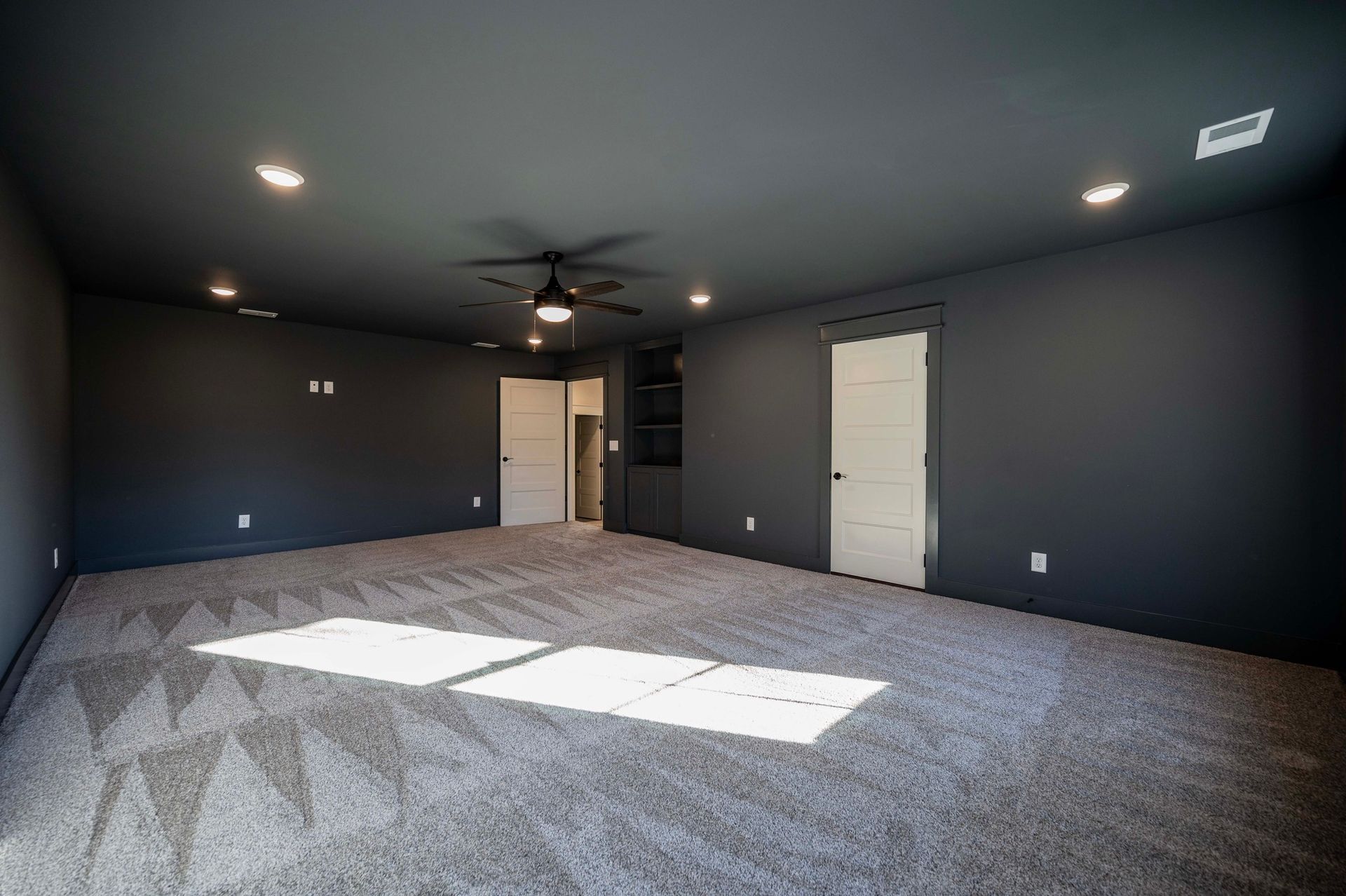 Empty room with gray walls and carpet. Two white doors, recessed lighting, and a ceiling fan.