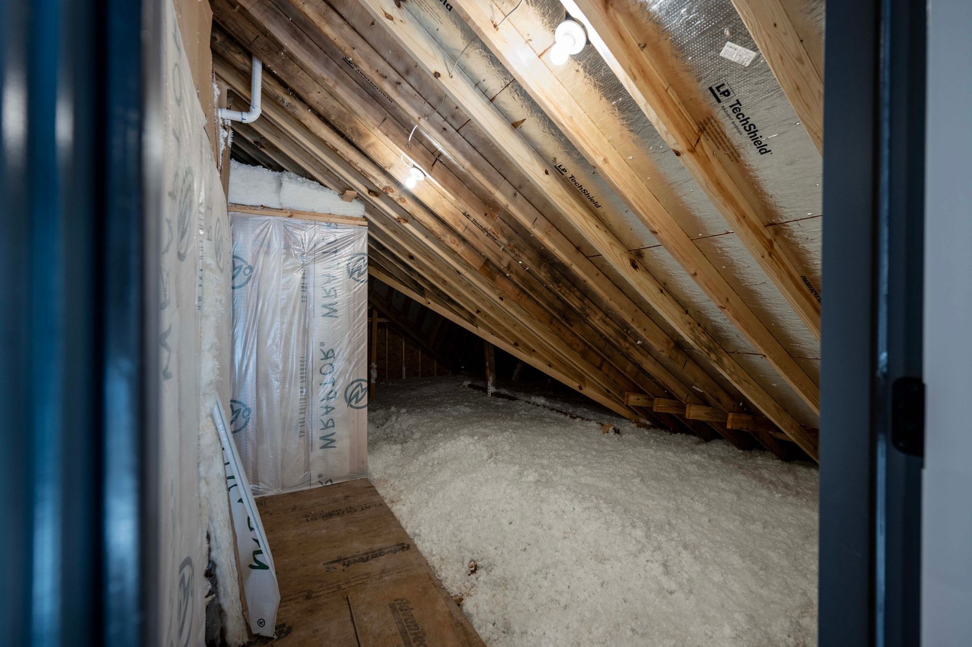 Attic with wood rafters, insulation, and a small enclosed area.