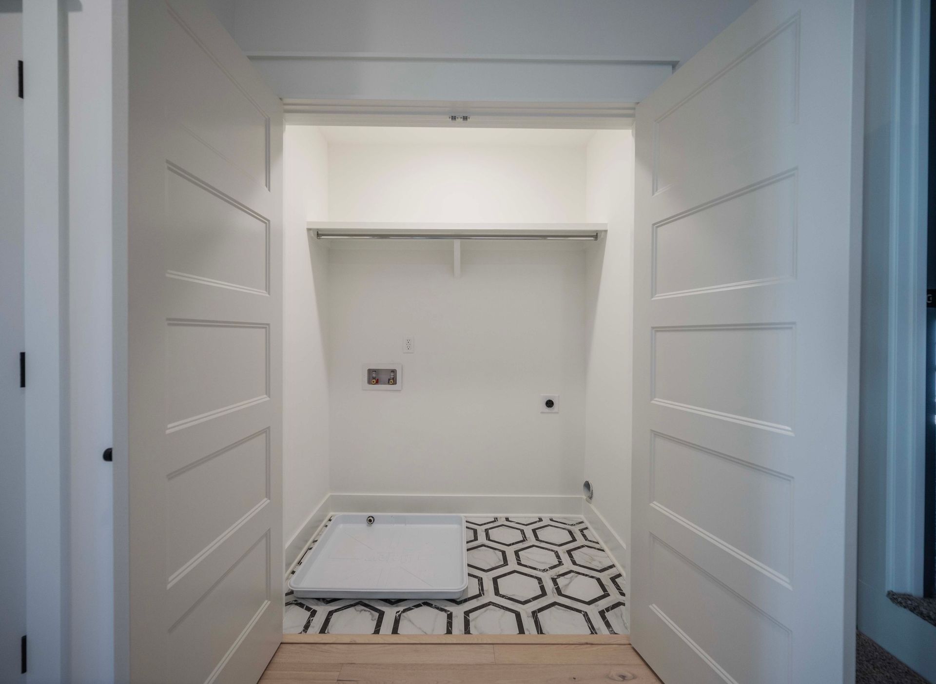 White closet with open doors; black and white patterned floor, shelf, and a utility panel.