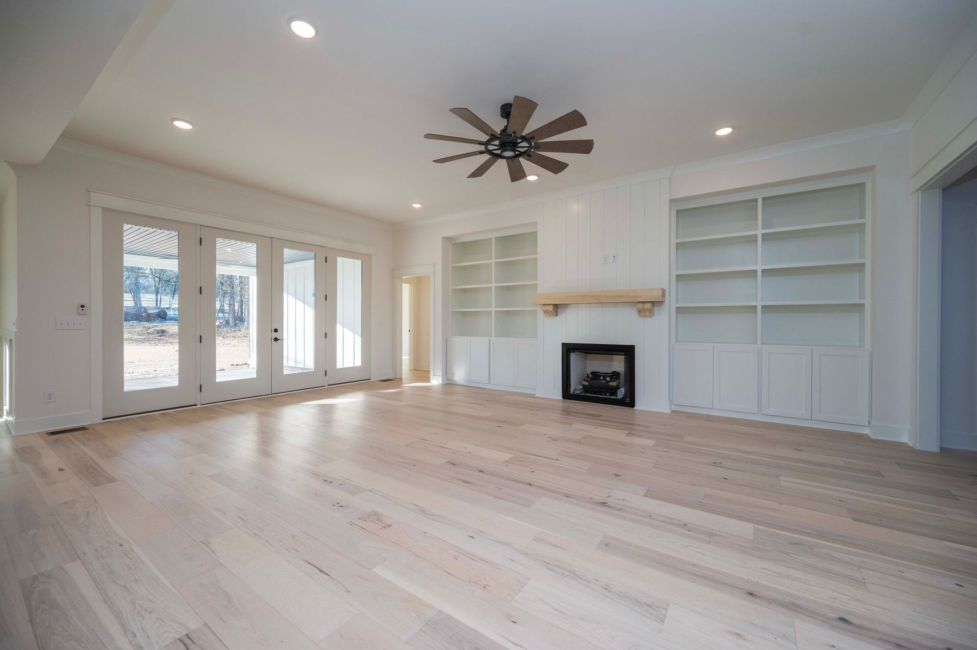 Empty living room with light wood floors, built-in bookshelves, fireplace, and glass doors.