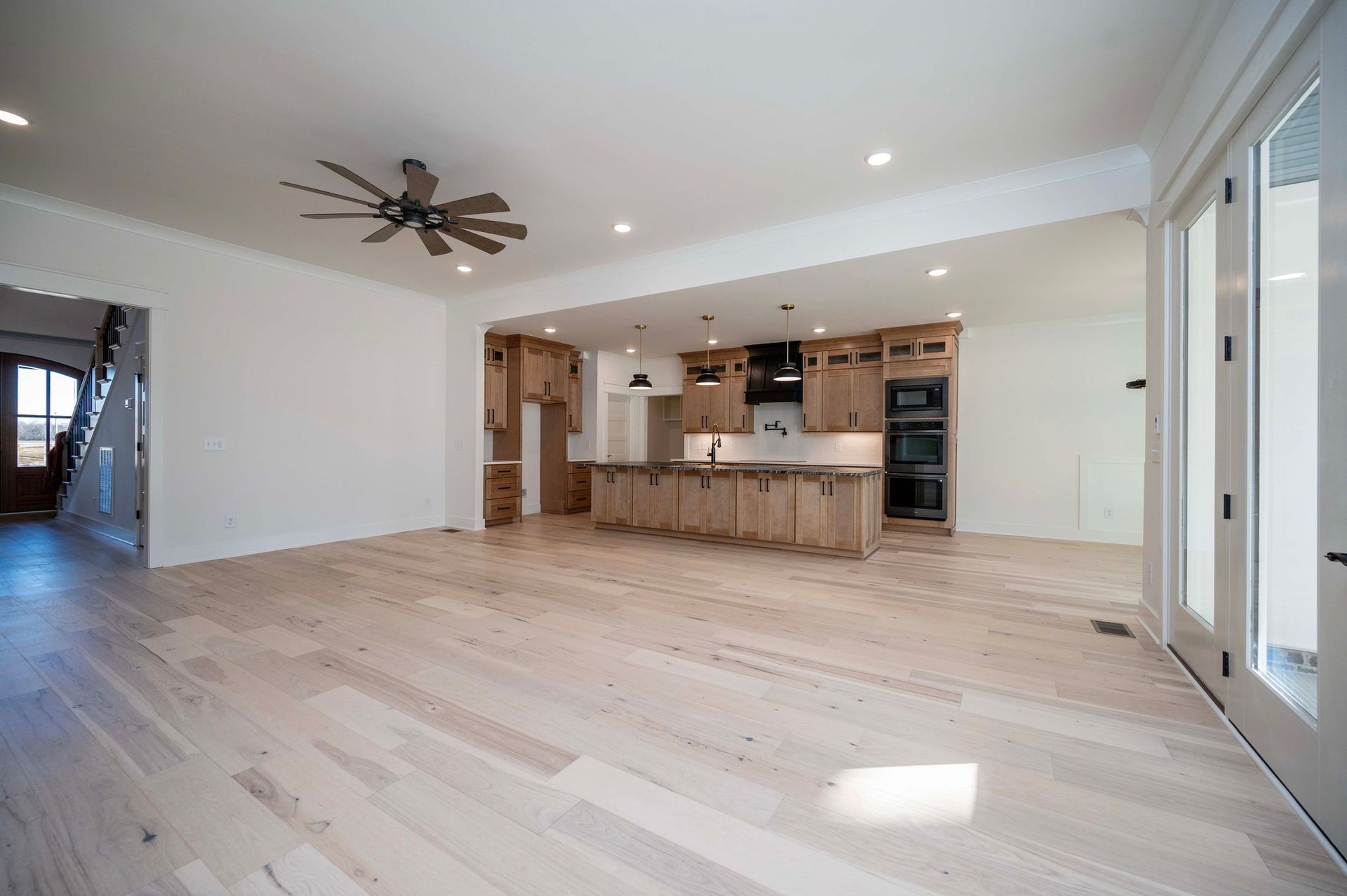 Empty modern kitchen with light wood floors, cabinets, and a kitchen island. A ceiling fan hangs above.