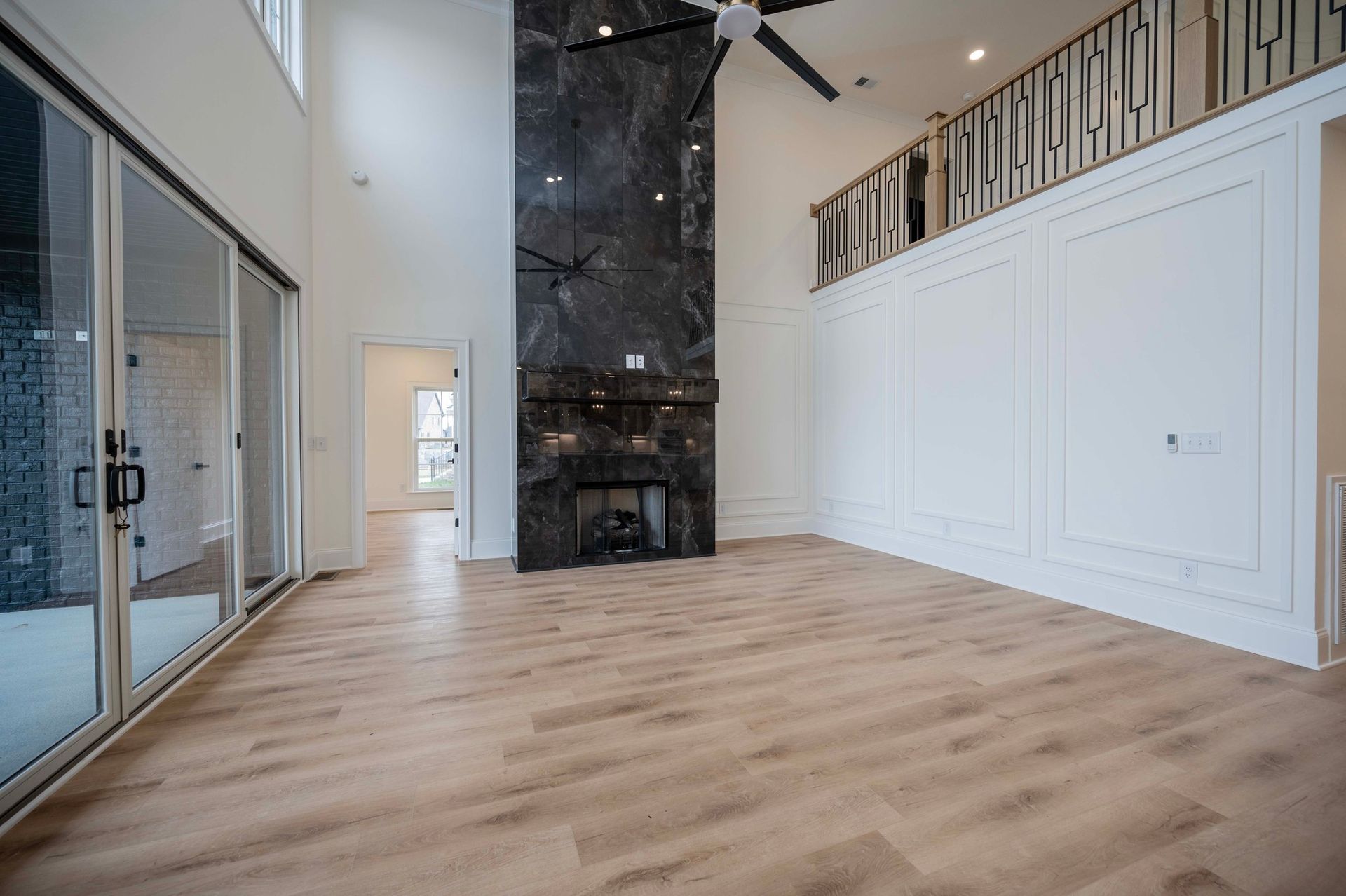 Empty modern living room with fireplace, sliding glass doors, and light wood flooring.