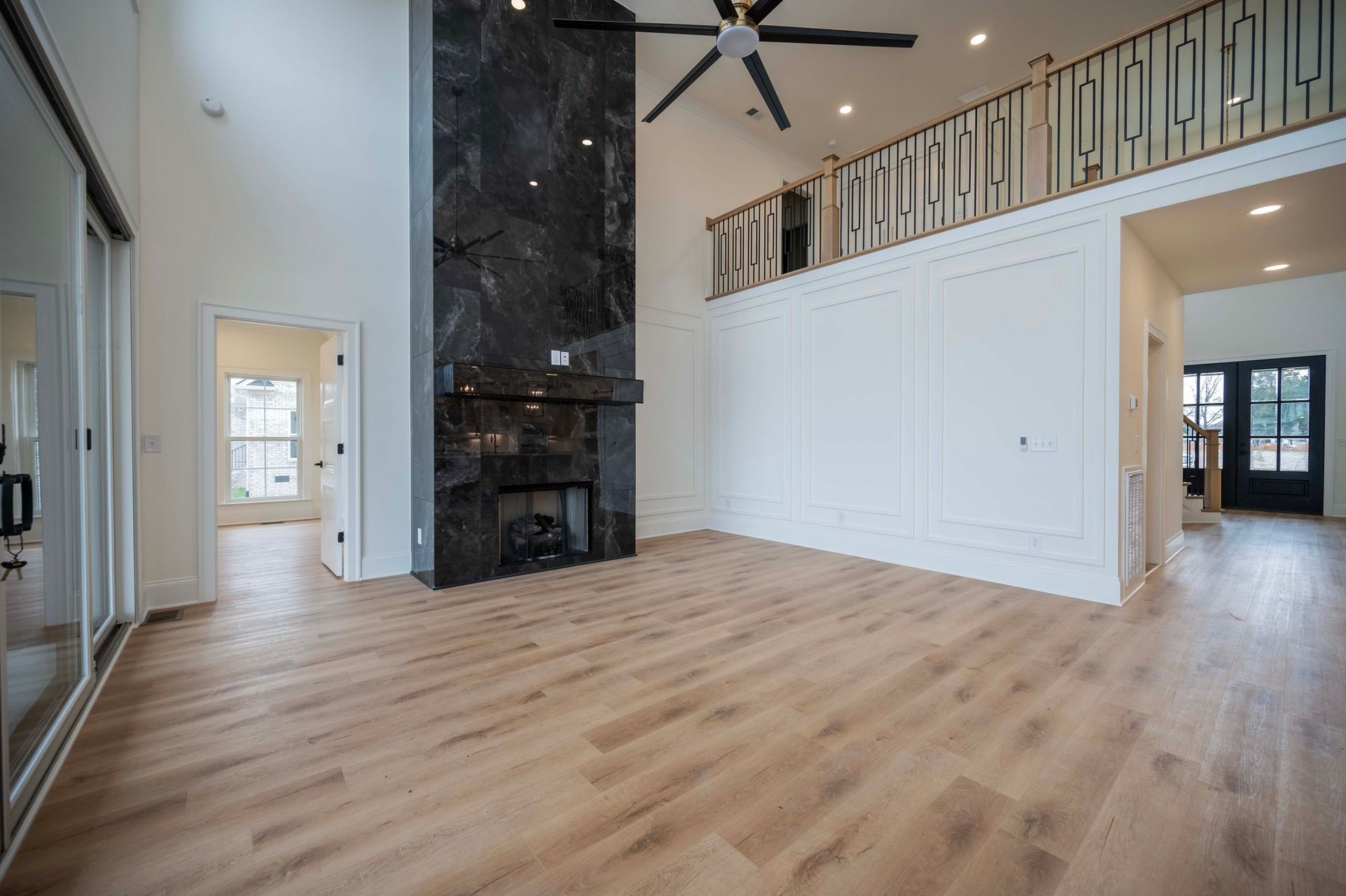 Spacious, empty living room with wood flooring, a fireplace, and a second-story balcony.