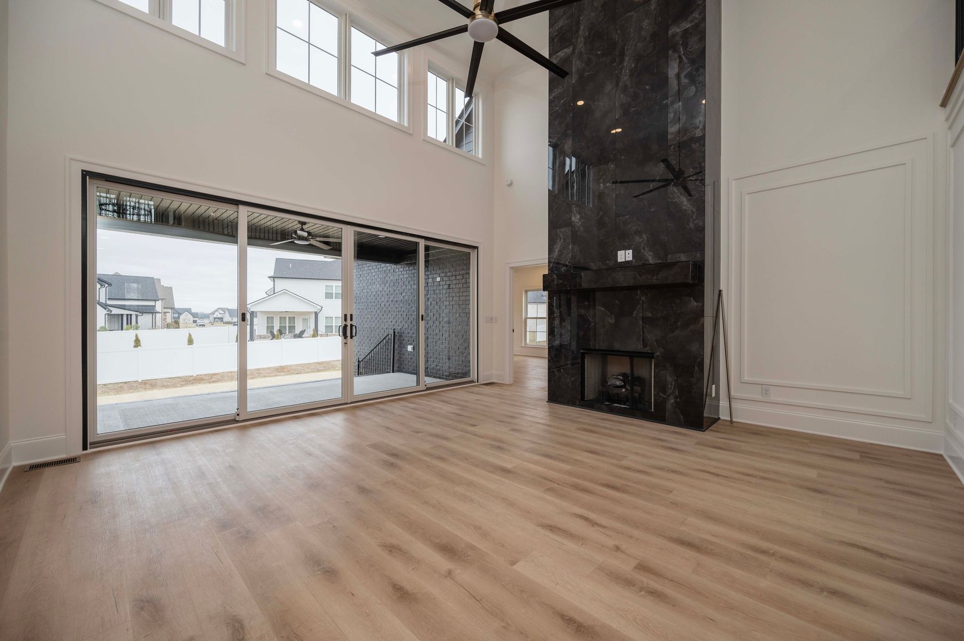 Empty, modern living room with large sliding doors, a fireplace, and light wood flooring.
