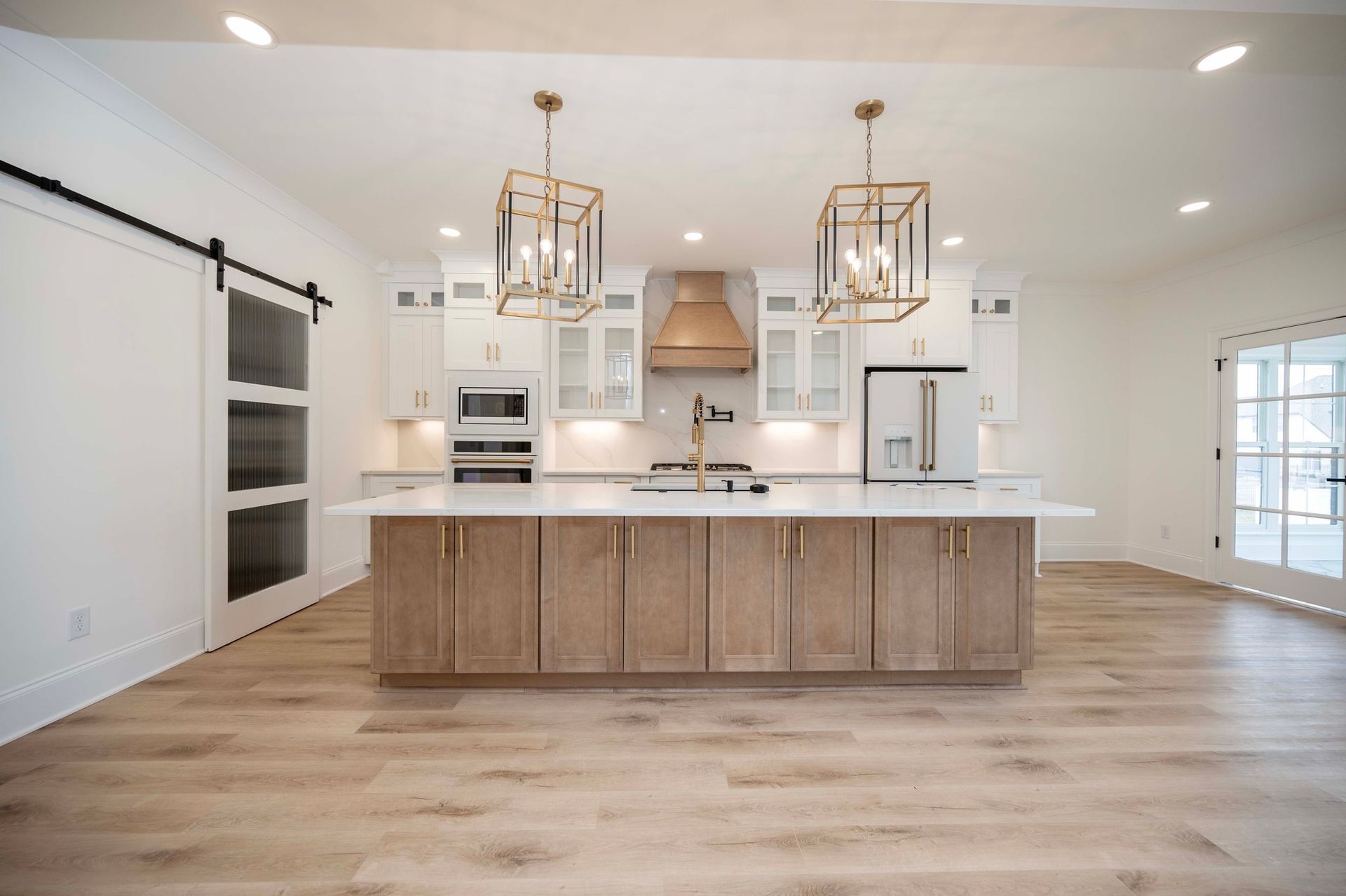 Modern kitchen with large island, light wood cabinets, and gold light fixtures.