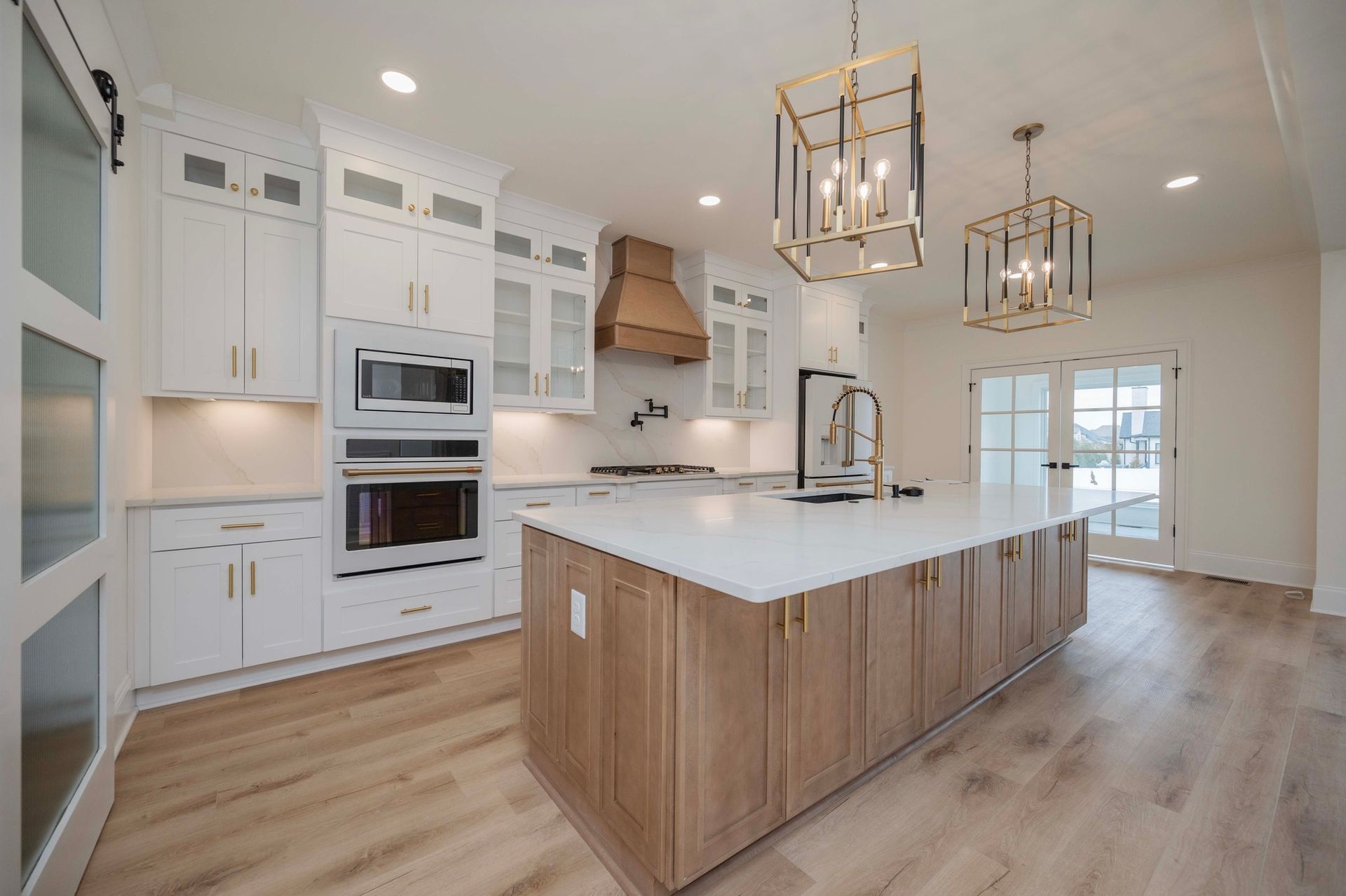 Modern kitchen with white cabinets, wood island, and gold light fixtures.