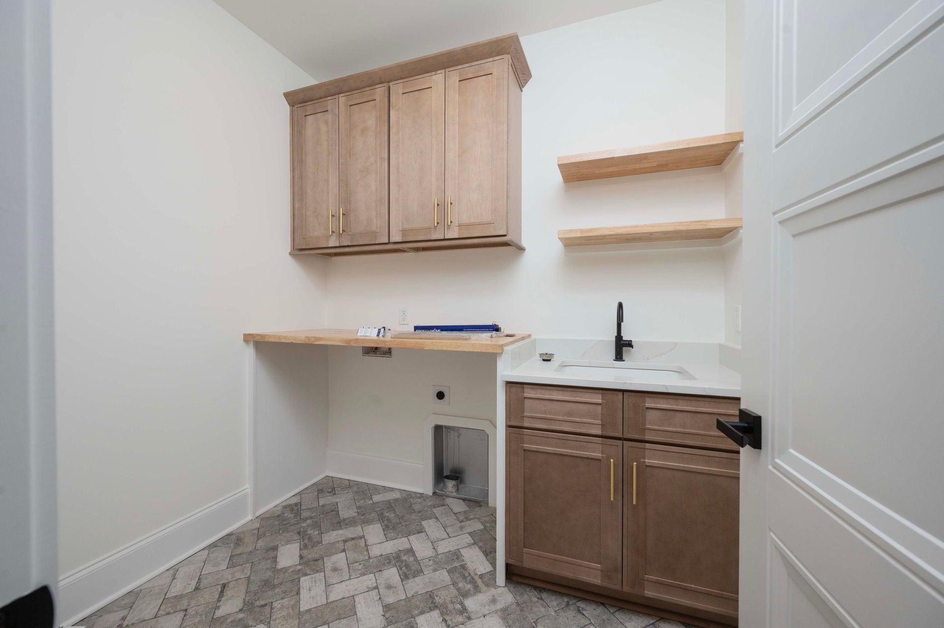 Laundry room with cabinets, sink, and shelves. Light wood tones and white walls. Gray patterned floor.