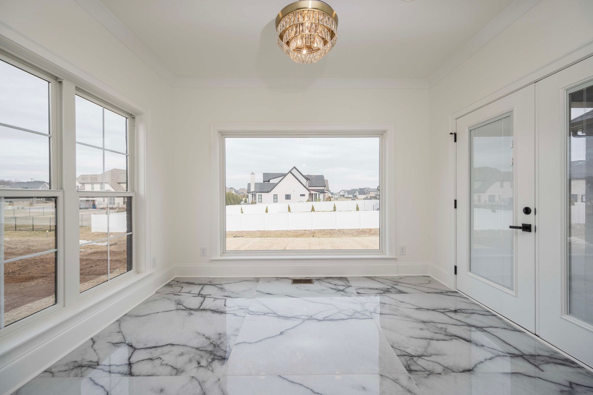 Bright room with marble floors, windows, and a view of a house. Crystal chandelier.
