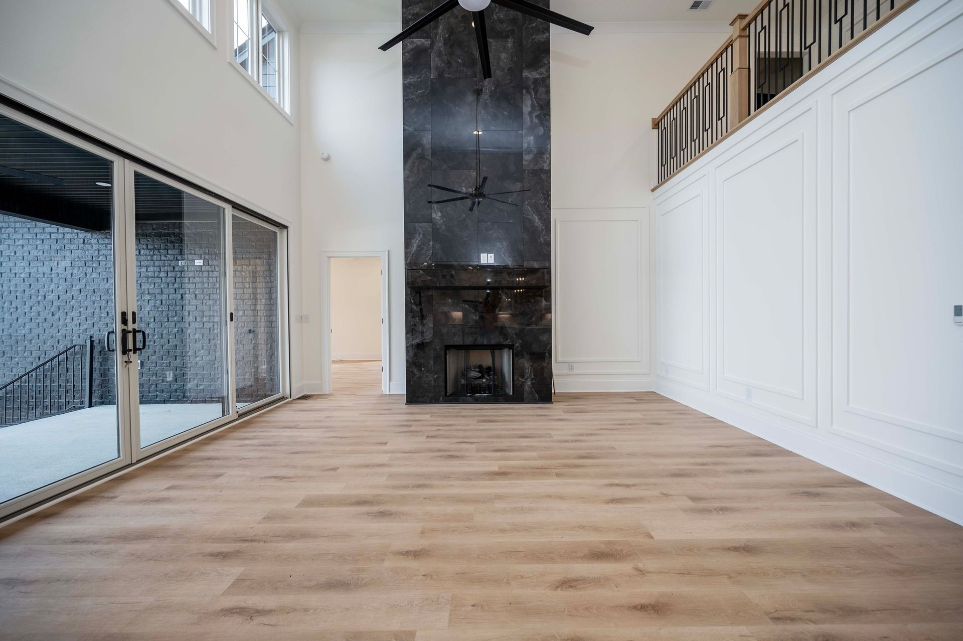 Empty living room with tall fireplace and large windows; light wood floors.