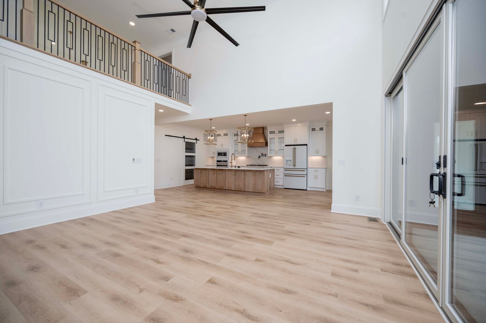 Open-concept living space with a kitchen, loft, and large windows.  Light wood floors and white walls.