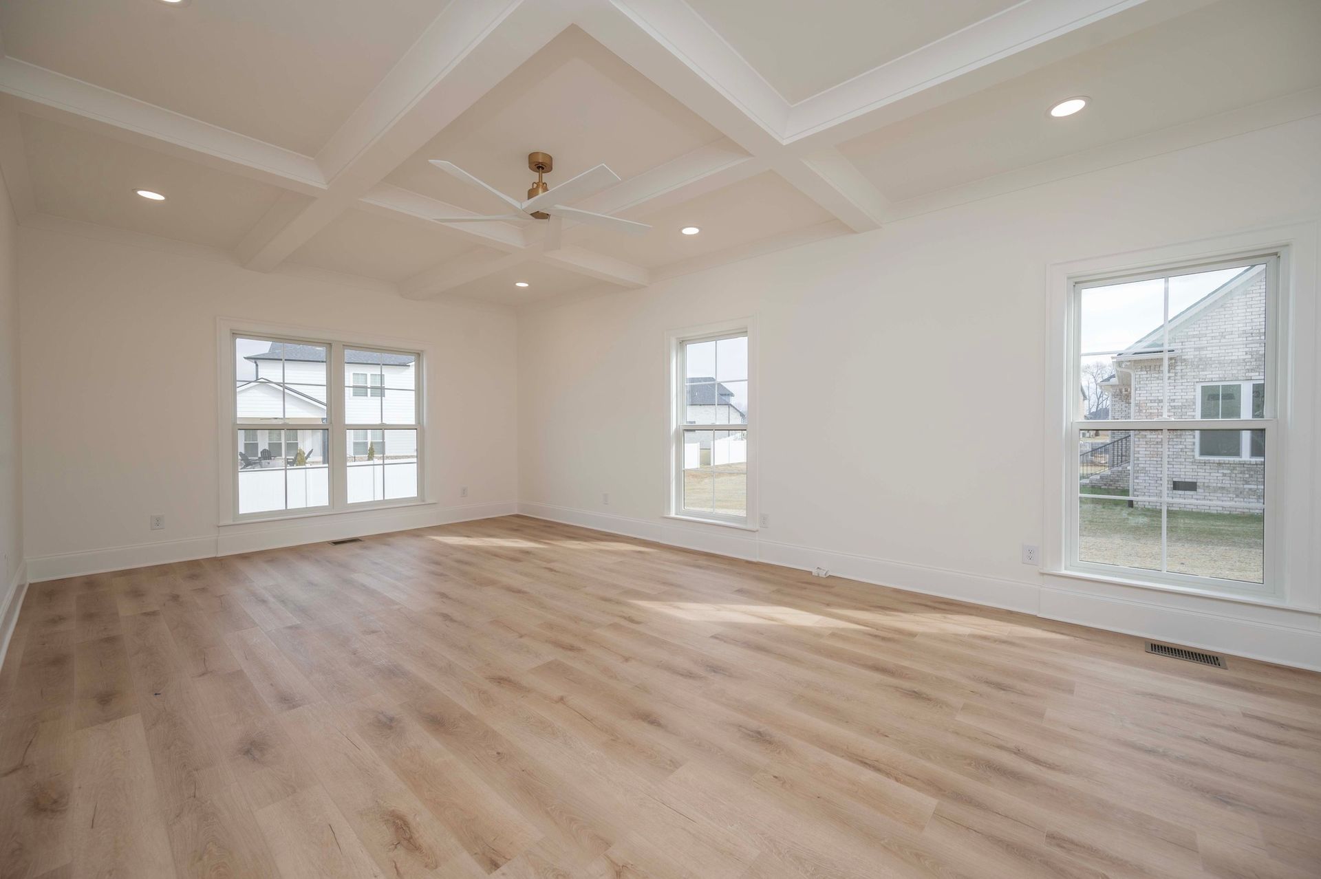 Empty bright room with wooden floor, white walls and ceiling, three windows, and ceiling fan.