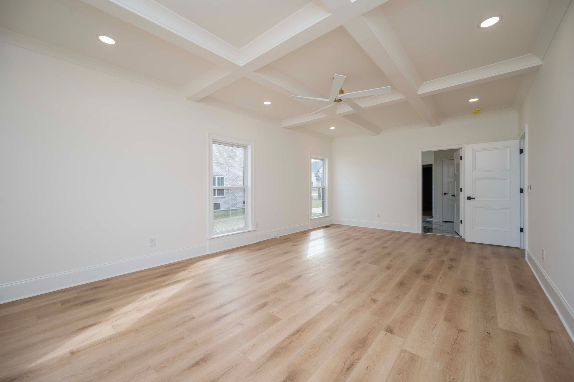 Empty room with light wood floors, white walls, and a coffered ceiling.