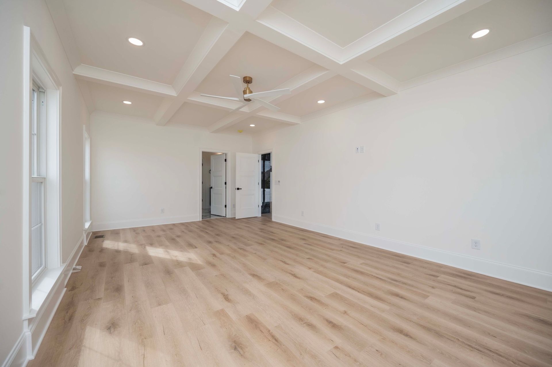 Empty, bright bedroom with wood flooring, white walls, and a coffered ceiling.