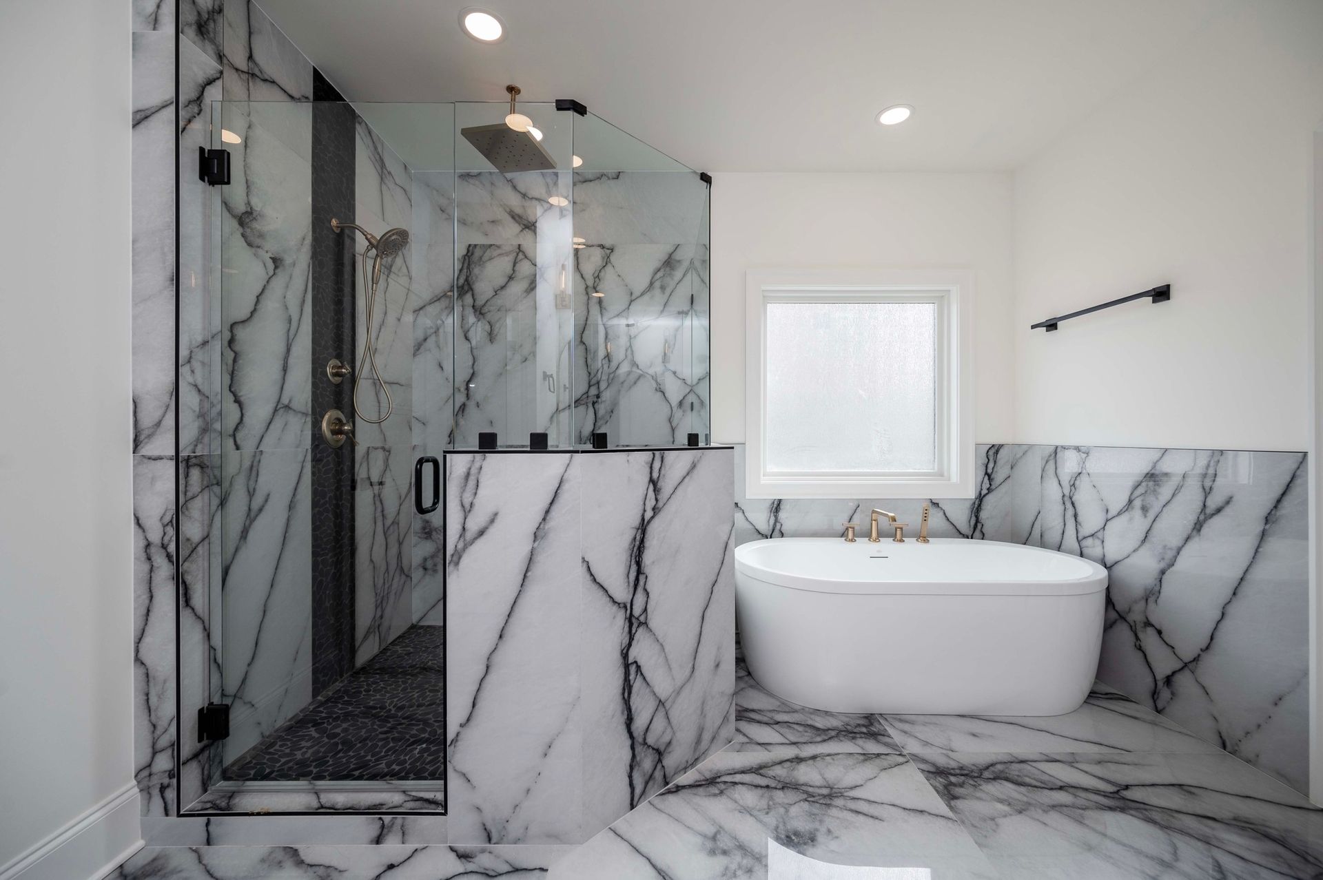 Luxurious bathroom with marble walls and shower, white soaking tub, glass shower door.