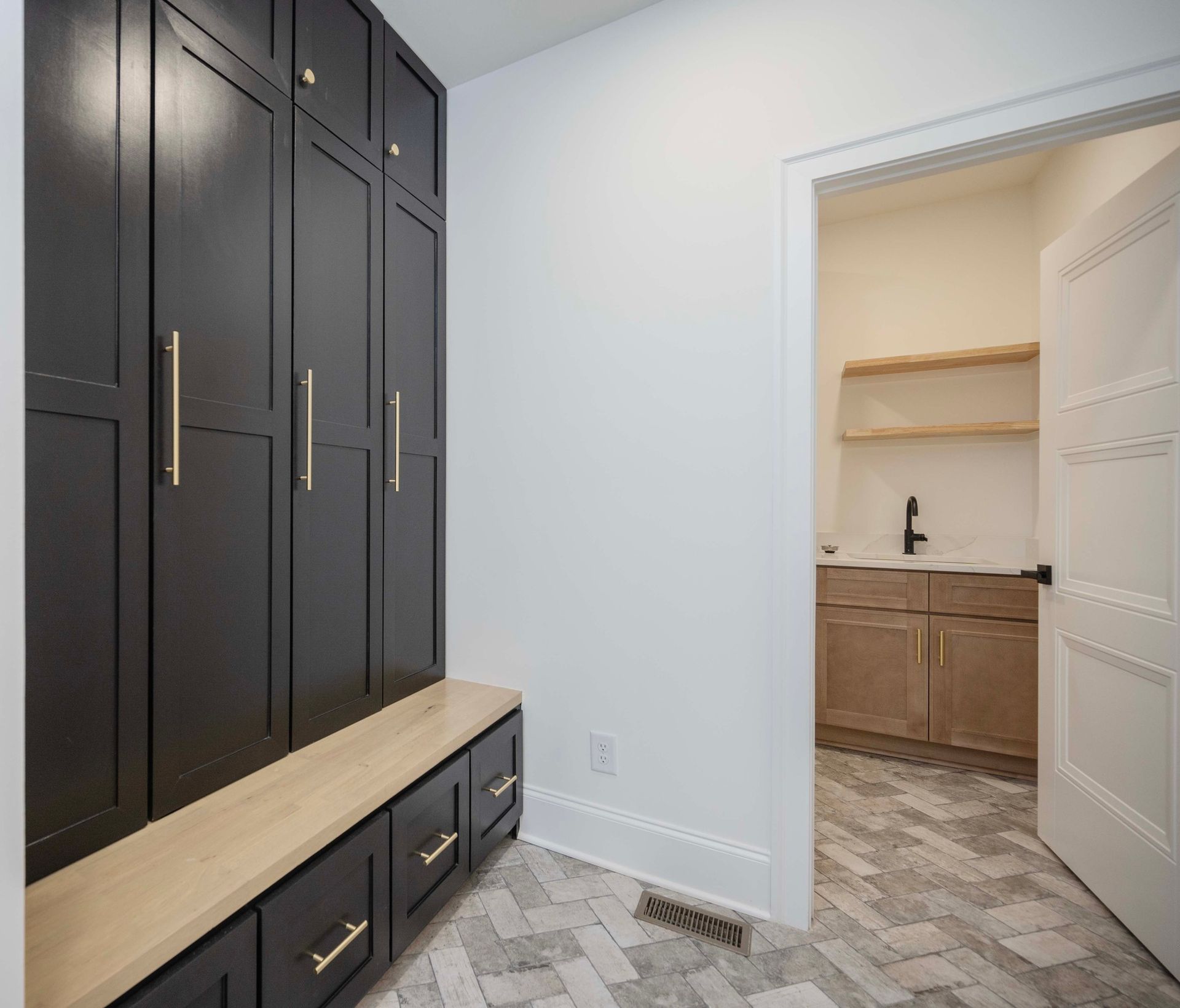 Dark cabinetry with gold hardware and bench in entryway, door to adjacent room.