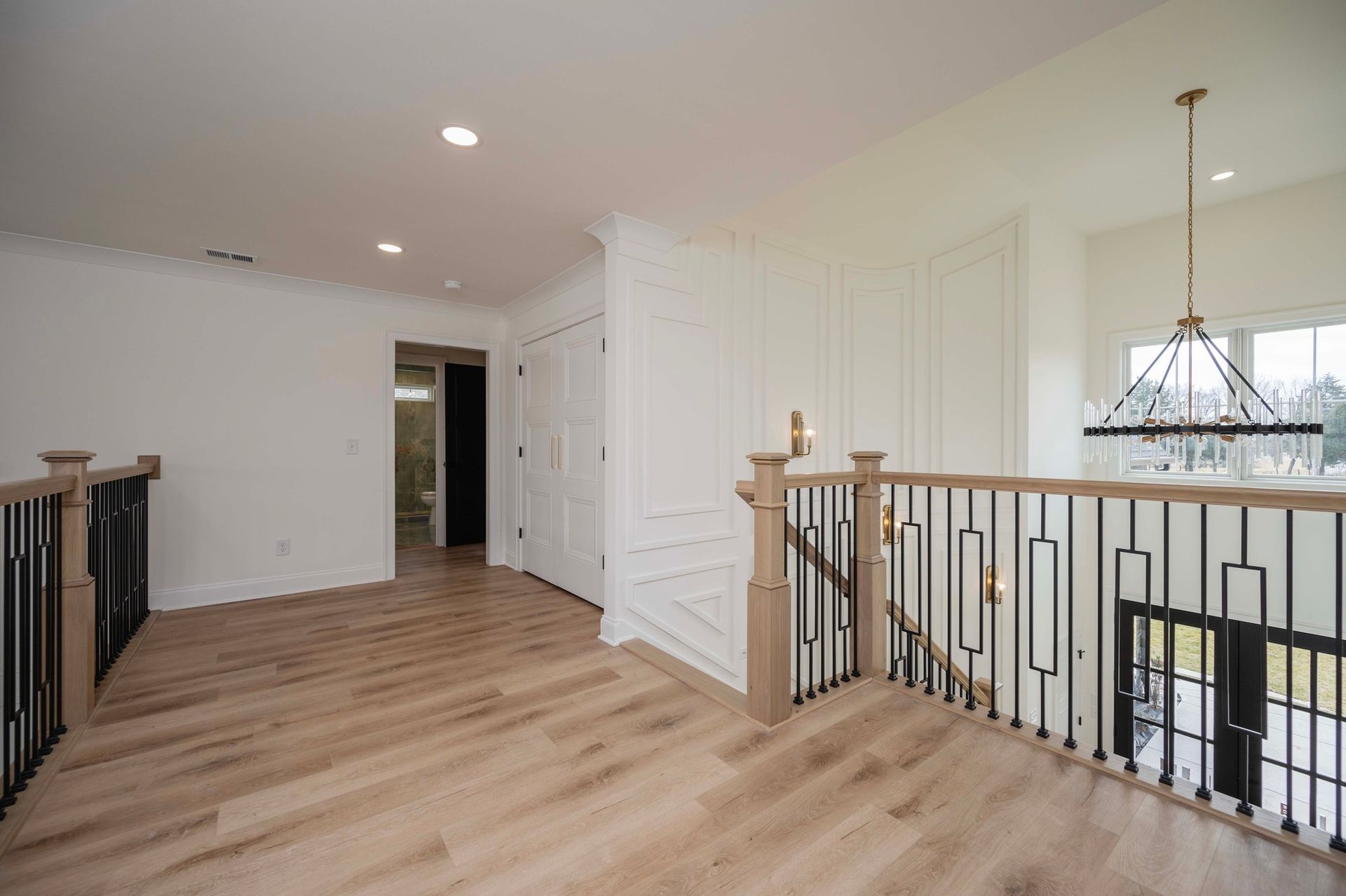 Interior of a second-floor hallway with light wood flooring, white walls, and a decorative railing.