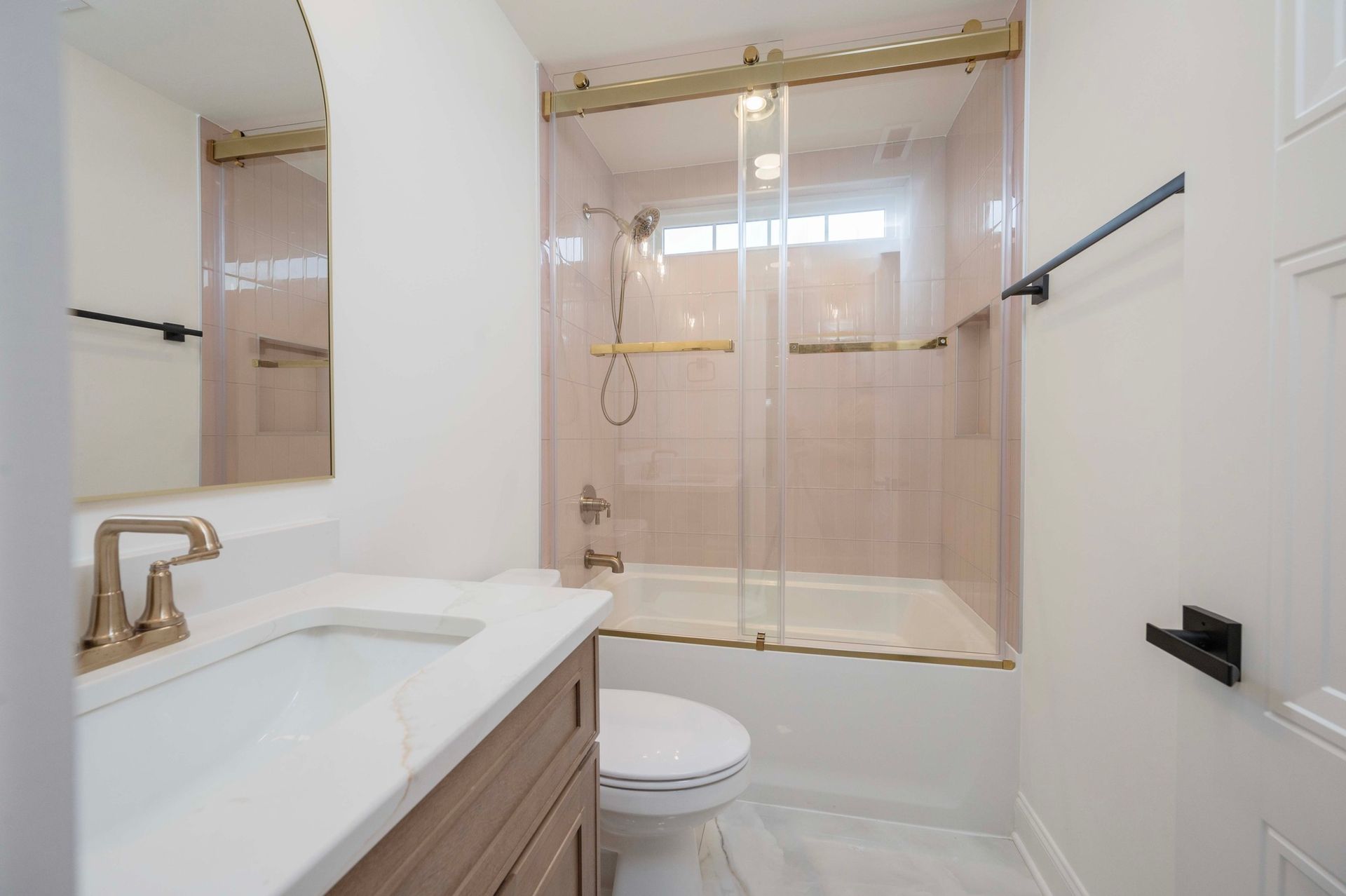 Bathroom with pink tiled shower, white countertop, gold fixtures, and a wooden vanity.