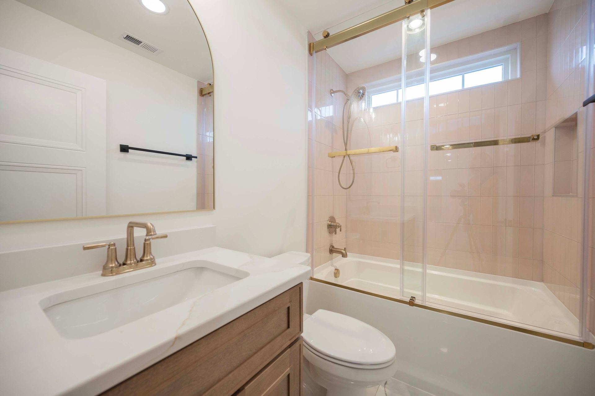 Bathroom with white sink, toilet, tub, gold fixtures, and pink tiled walls.