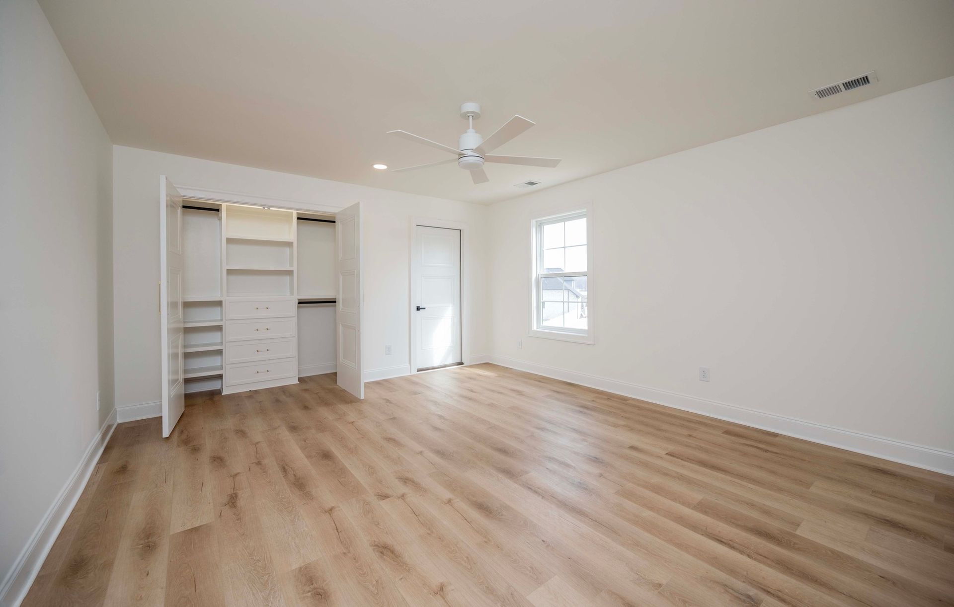 Empty bedroom with light wood floors, white walls, closet, and ceiling fan.