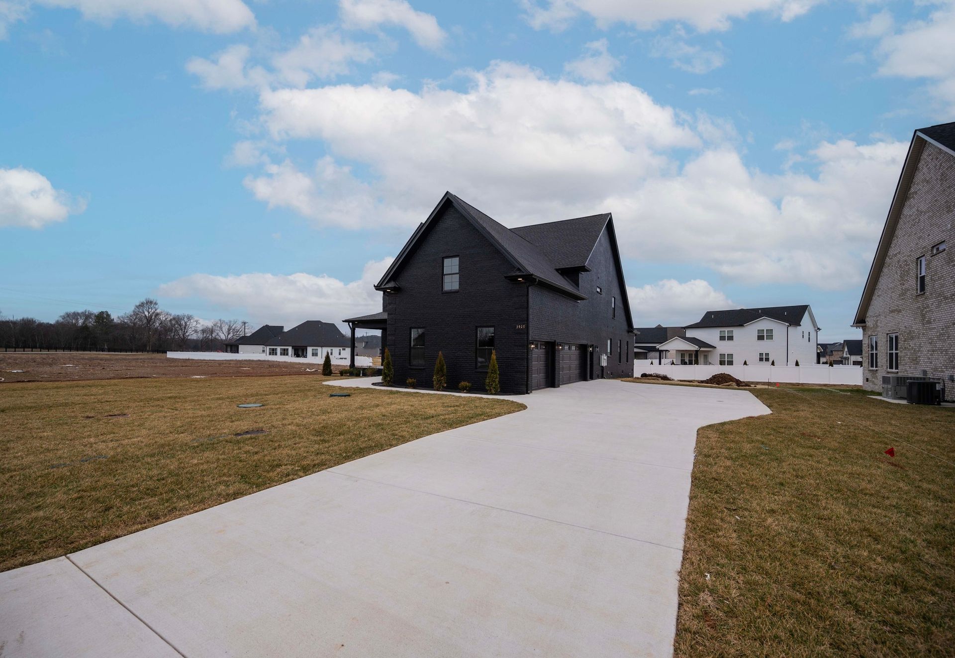 Black house with gray driveway on a sunny day. Other houses are visible in the distance.