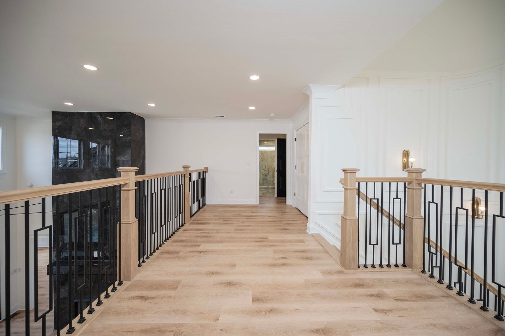 Hallway with light wood floors, a black and wood railing, and a dark stone wall.