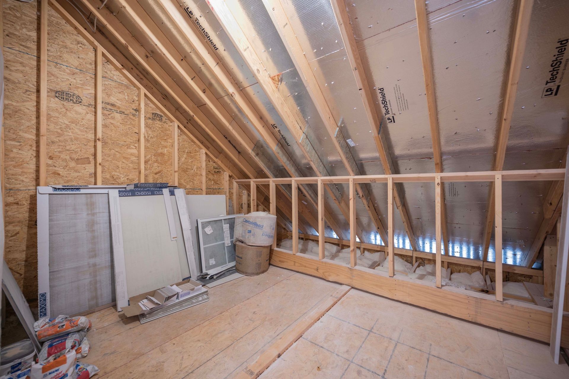 Interior view of unfinished attic with wooden beams, insulation, and building materials.