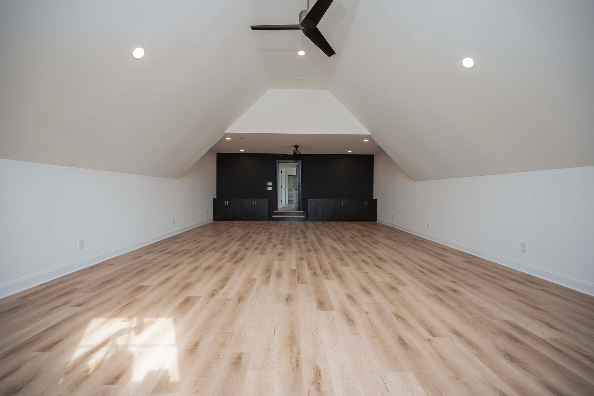 Empty, modern room with light wood floors, white walls, and a black ceiling fan.