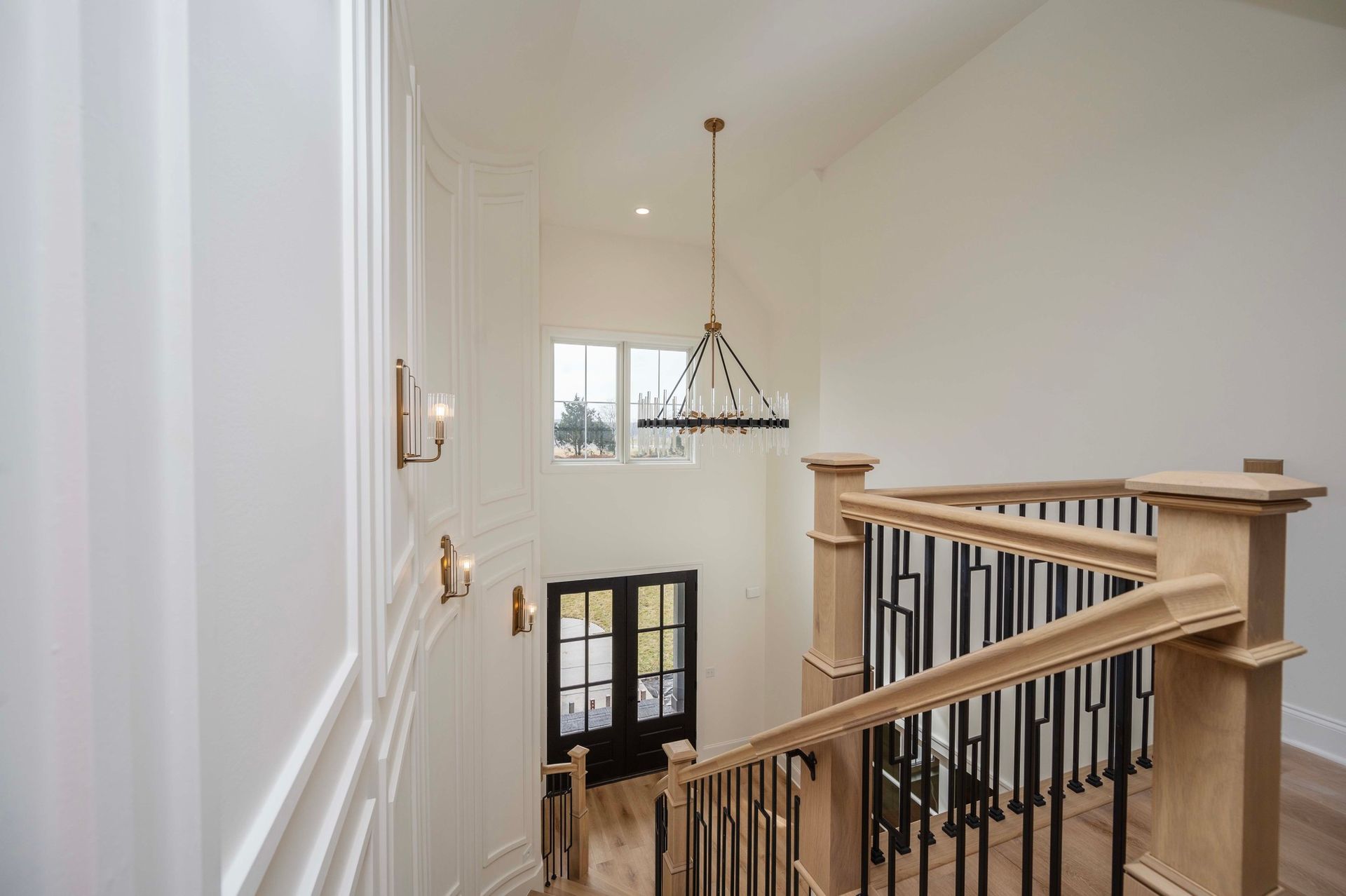 View of a two-story entryway with a chandelier, stairs, and a front door. White walls, wood banister.