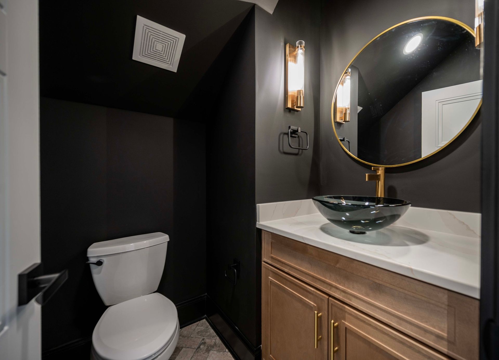 Small powder room with black walls, a light wood vanity, and a gold-framed mirror.