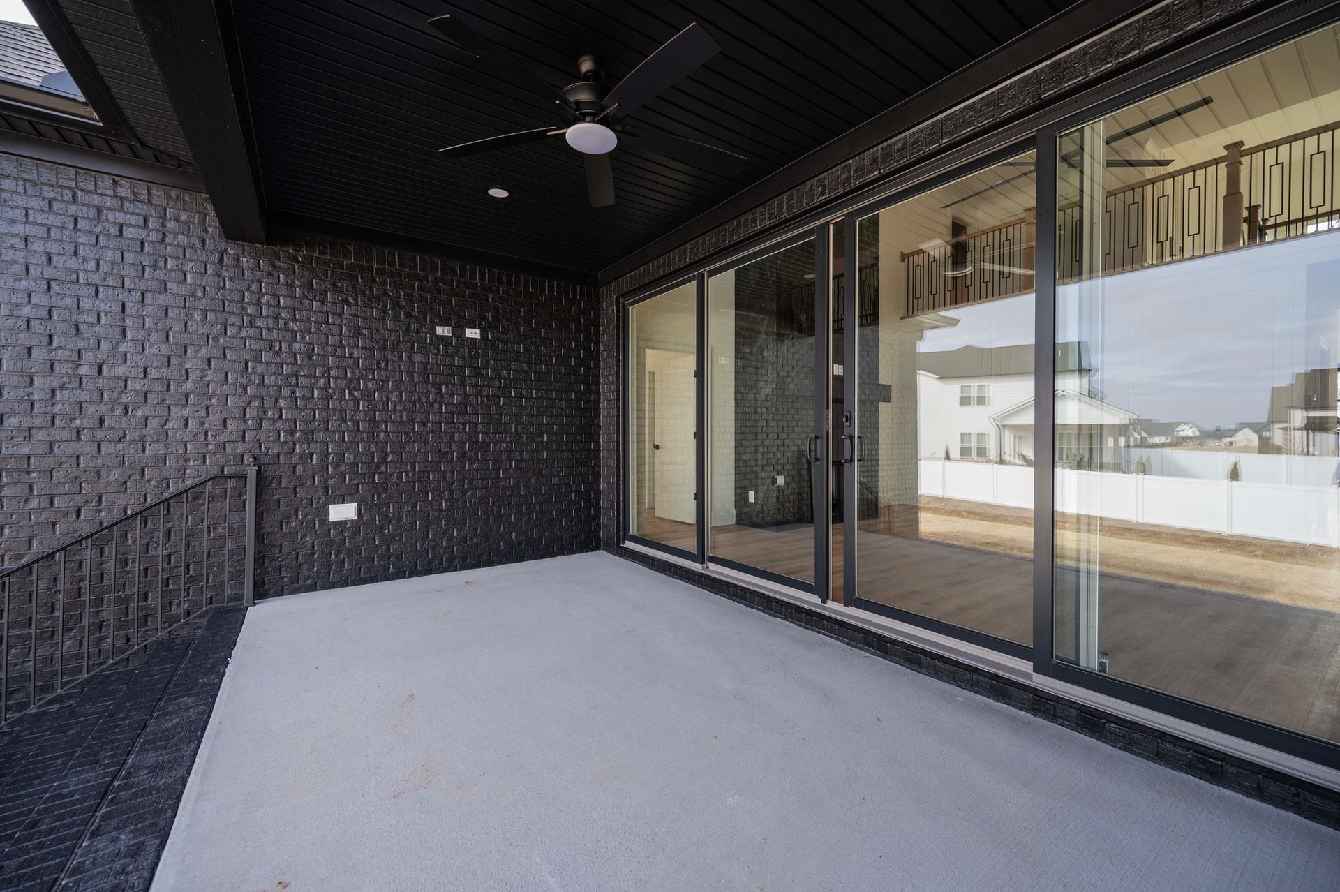 Covered patio with black brick wall, gray concrete floor, and large glass sliding doors.
